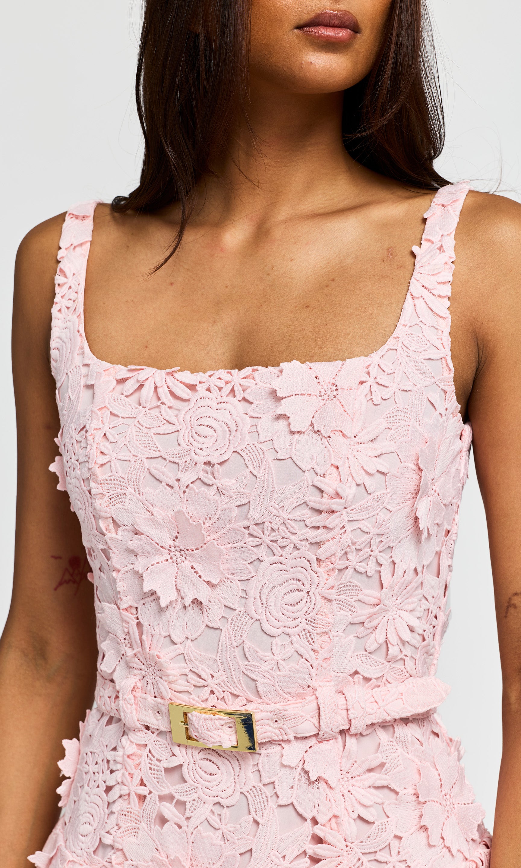Close-up of a pink lace dress with a belt on a plain background