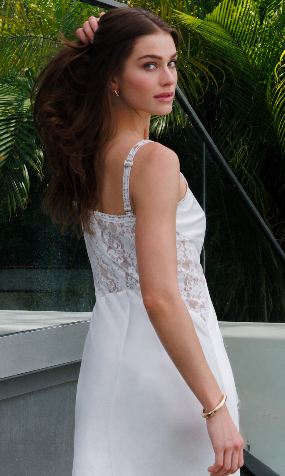 Woman in a white lace dress standing outdoors with greenery in the background