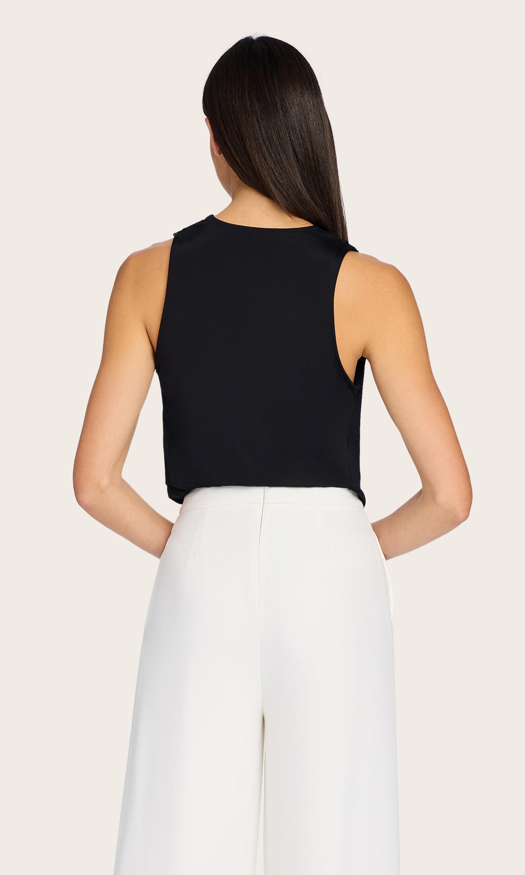The model pairs the Ansel Bodysuit in black with white wide-leg pants in this rear view image, capturing a polished warm-weather look.