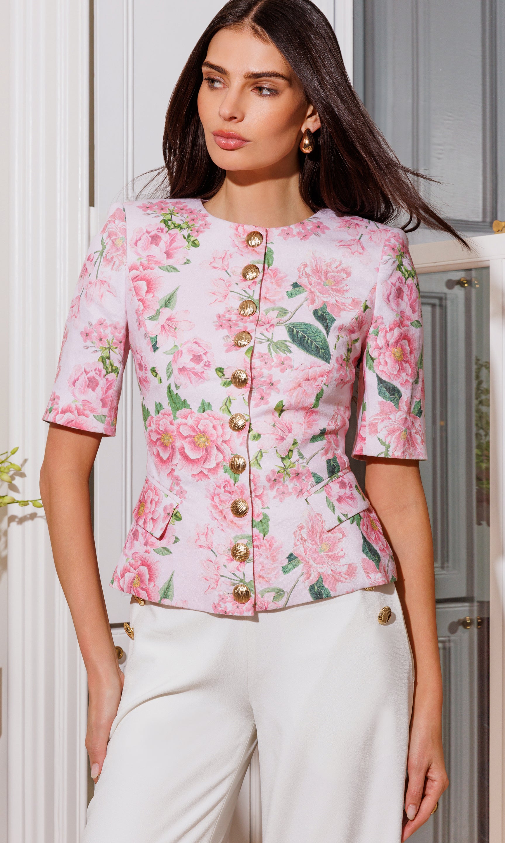 Model wears the Adriana Floral Linen Jacket in pink petal dream in a close-up front view, highlighting the tailored waist, short sleeves, and statement gold buttons over the floral print.