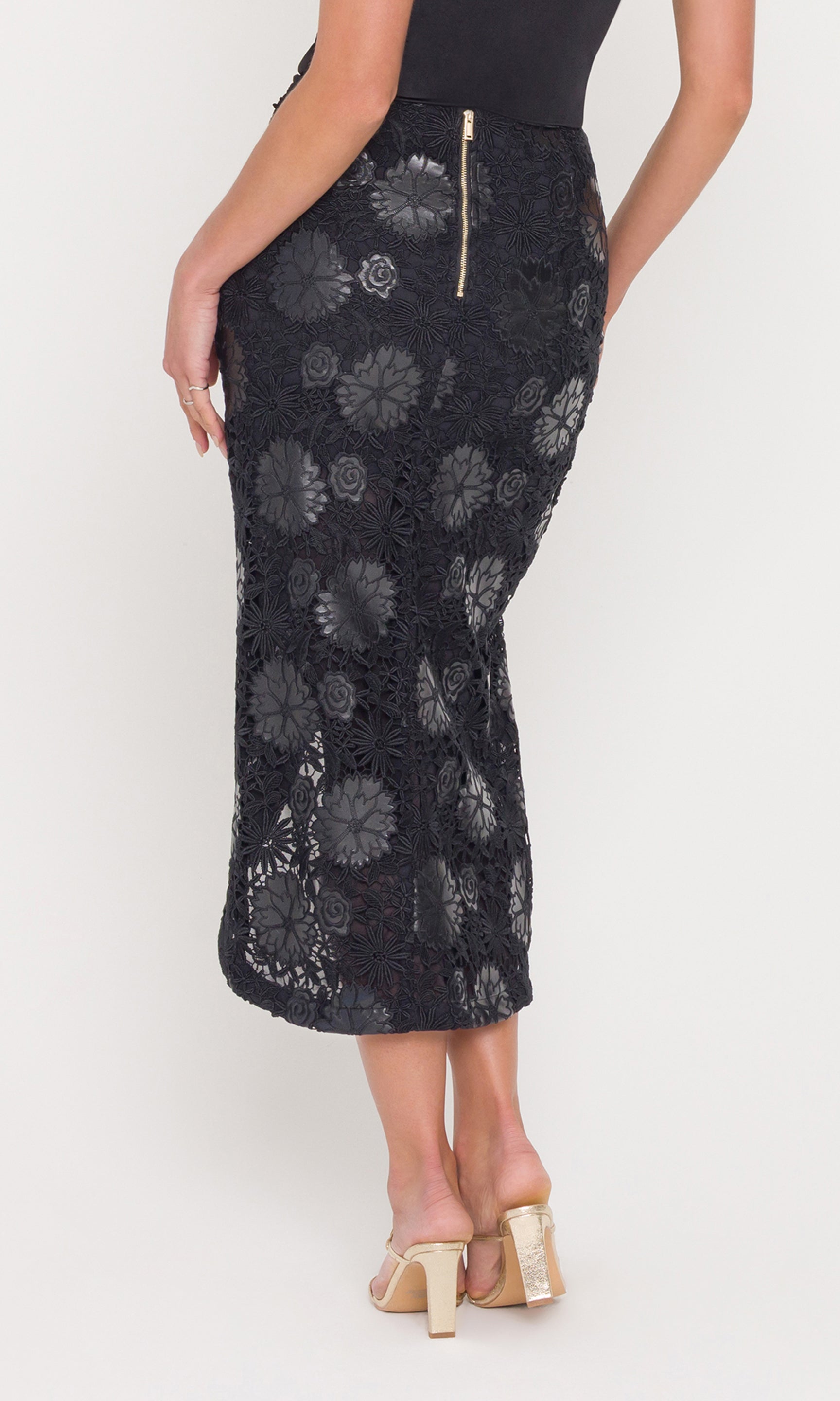 Back view of model wearing a black vegan leather lace skirt with a black cami on a white background