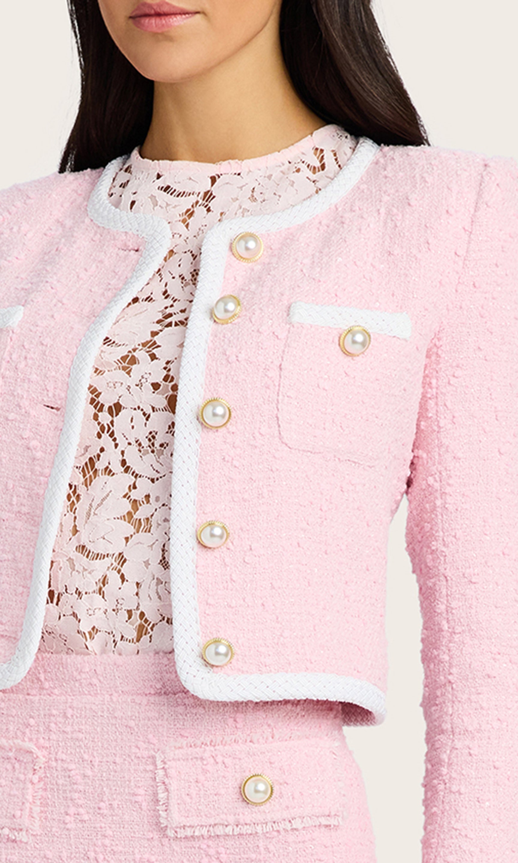 detailed view of model wearing a light pink Amber tweed jacket with pearl buttons, paired with a matching light pink tweed skirt, and a light pink lace under shirt
