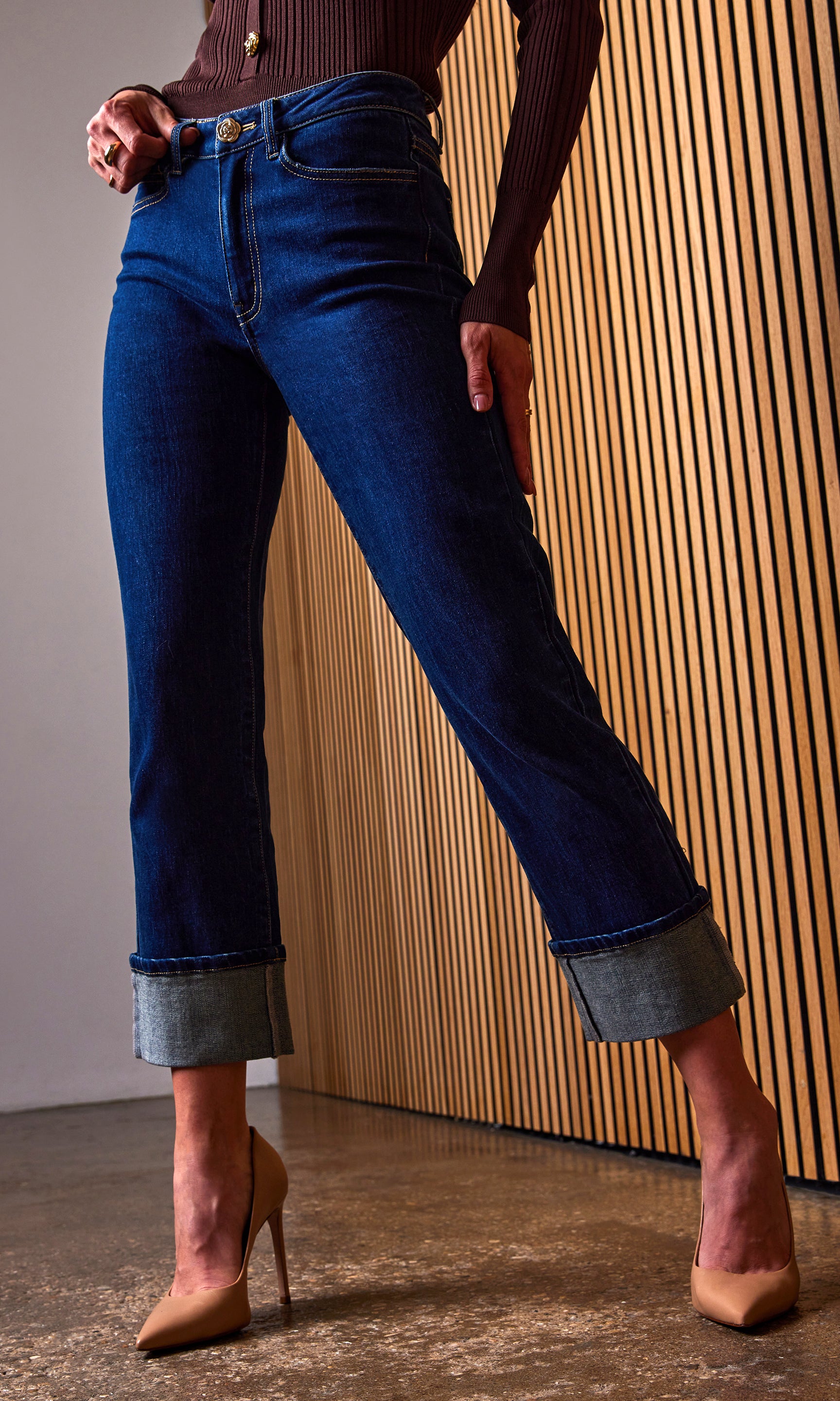 Person wearing blue jeans with a wooden panel background