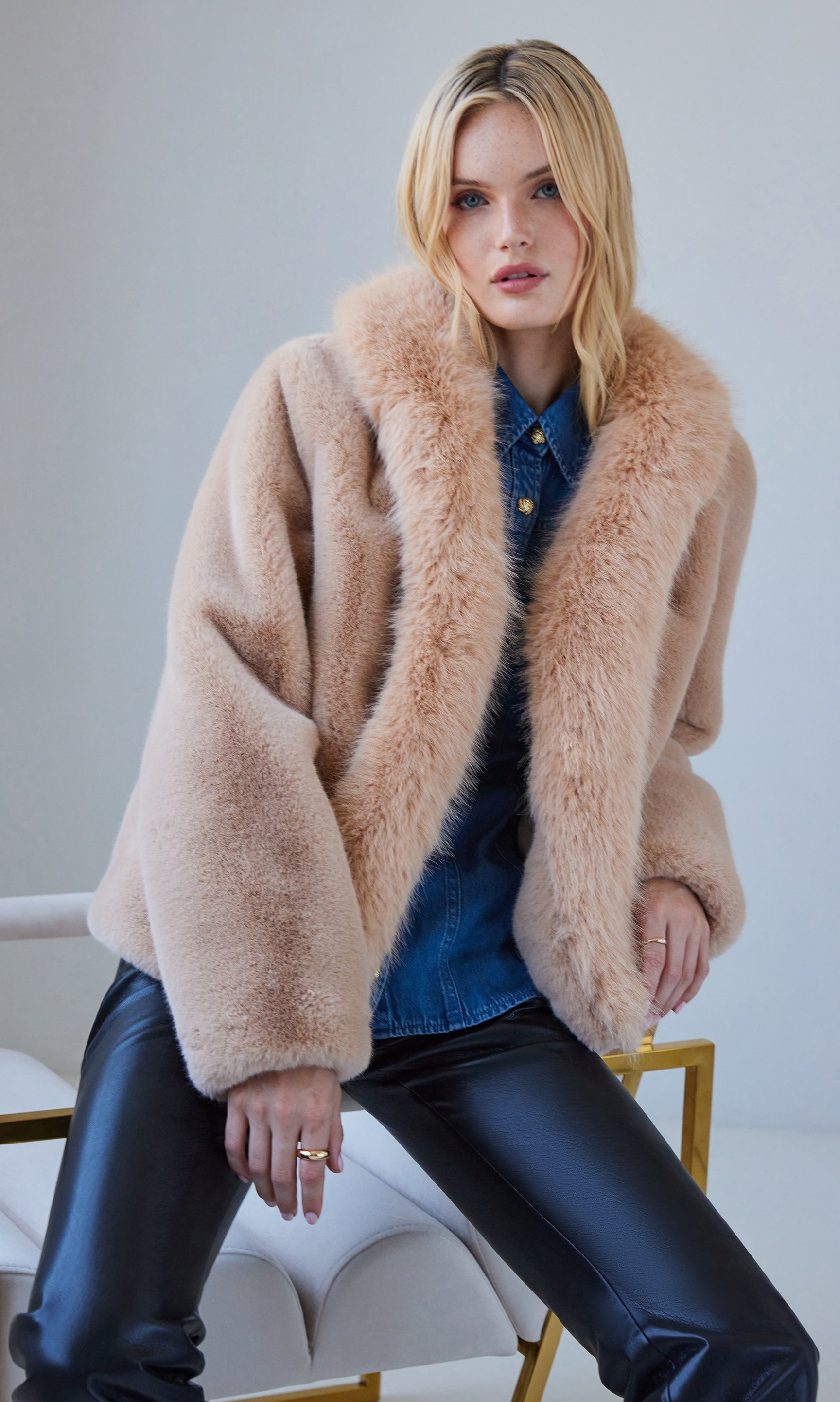 Front view of the Dasha Faux Fur Jacket in beige, worn over a blue top with black leather pants, creating a chic winter look.