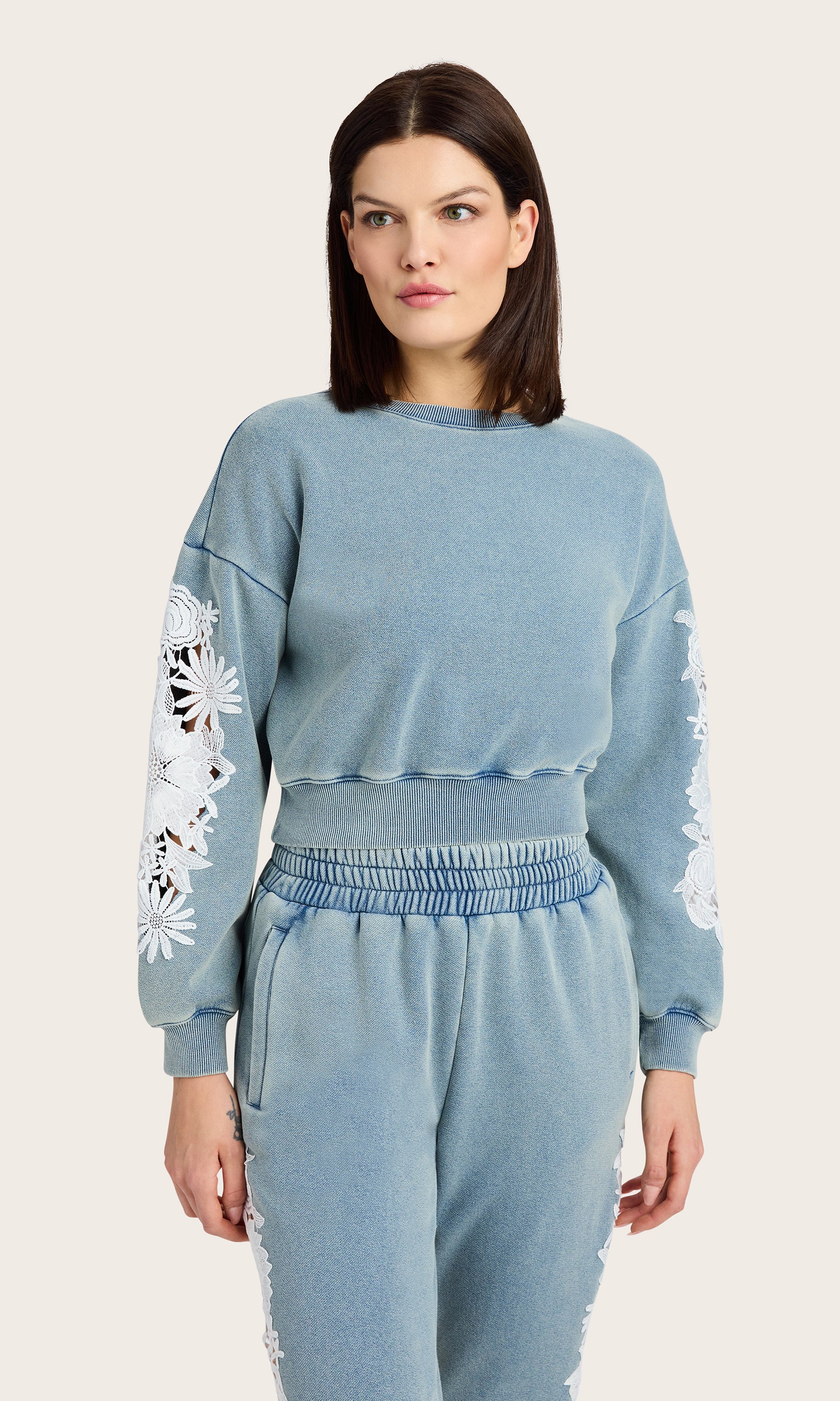 front view of model wearing the Arabella washed denim sweatshirt with white lace details on the sleeves, paired with matching washed denim joggers