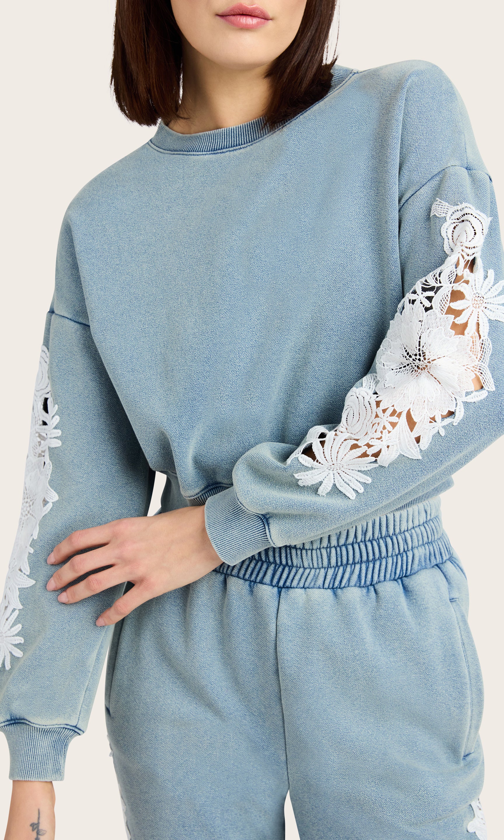 detailed view of model wearing the Arabella washed denim sweatshirt with white lace details on the sleeves, paired with matching washed denim joggers