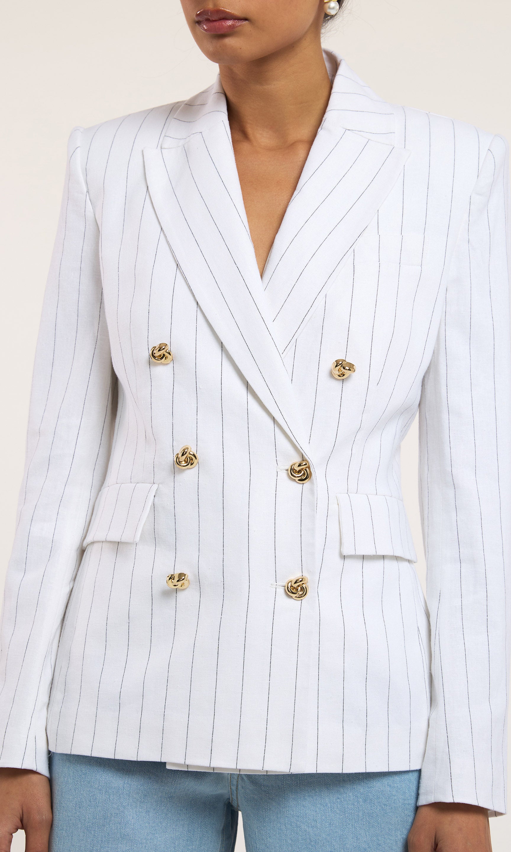 White pinstripe blazer with gold buttons worn by a person against a neutral background