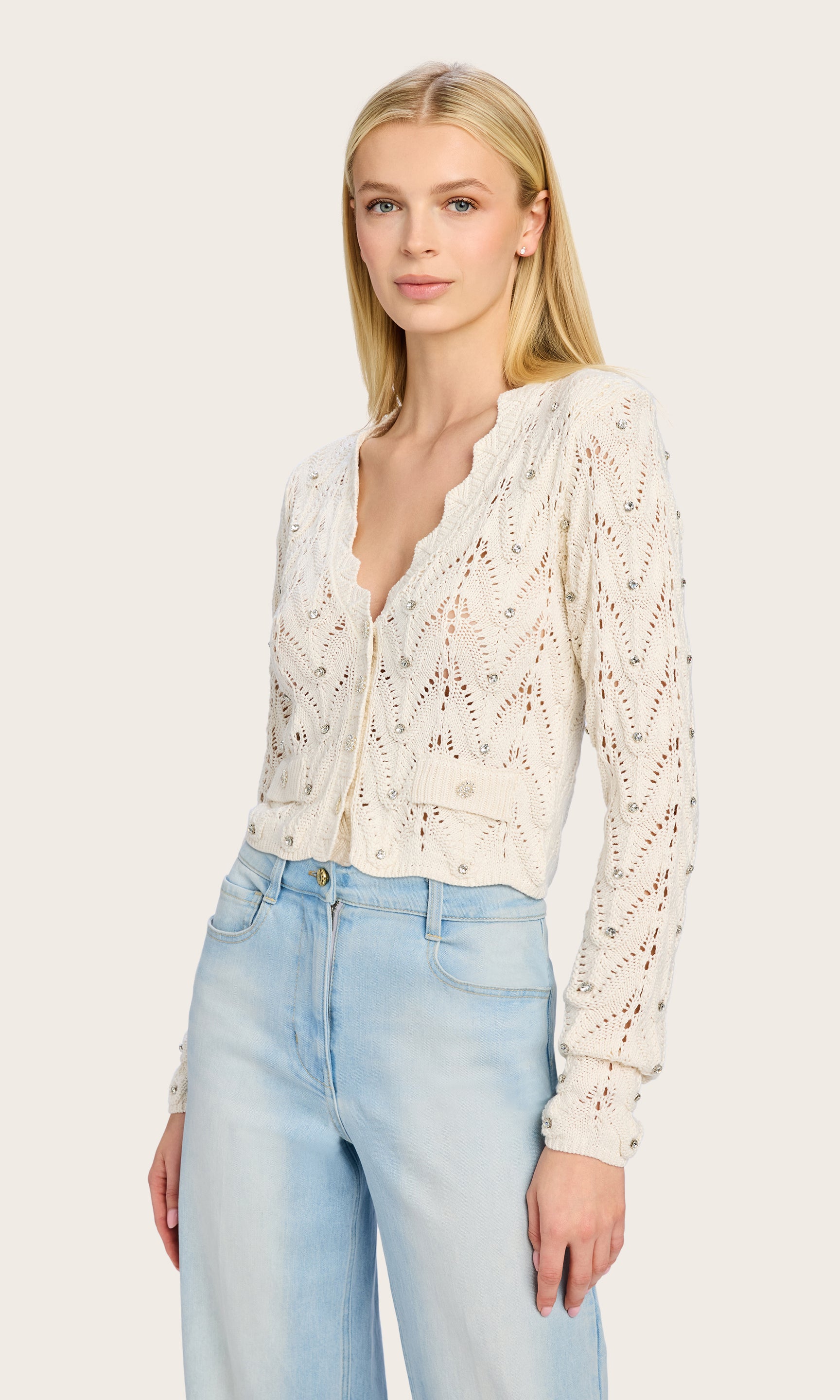 Side angle of the Blake Crystal Pointelle Cardigan as the model poses with a raffia clutch, completing a chic and casual look.