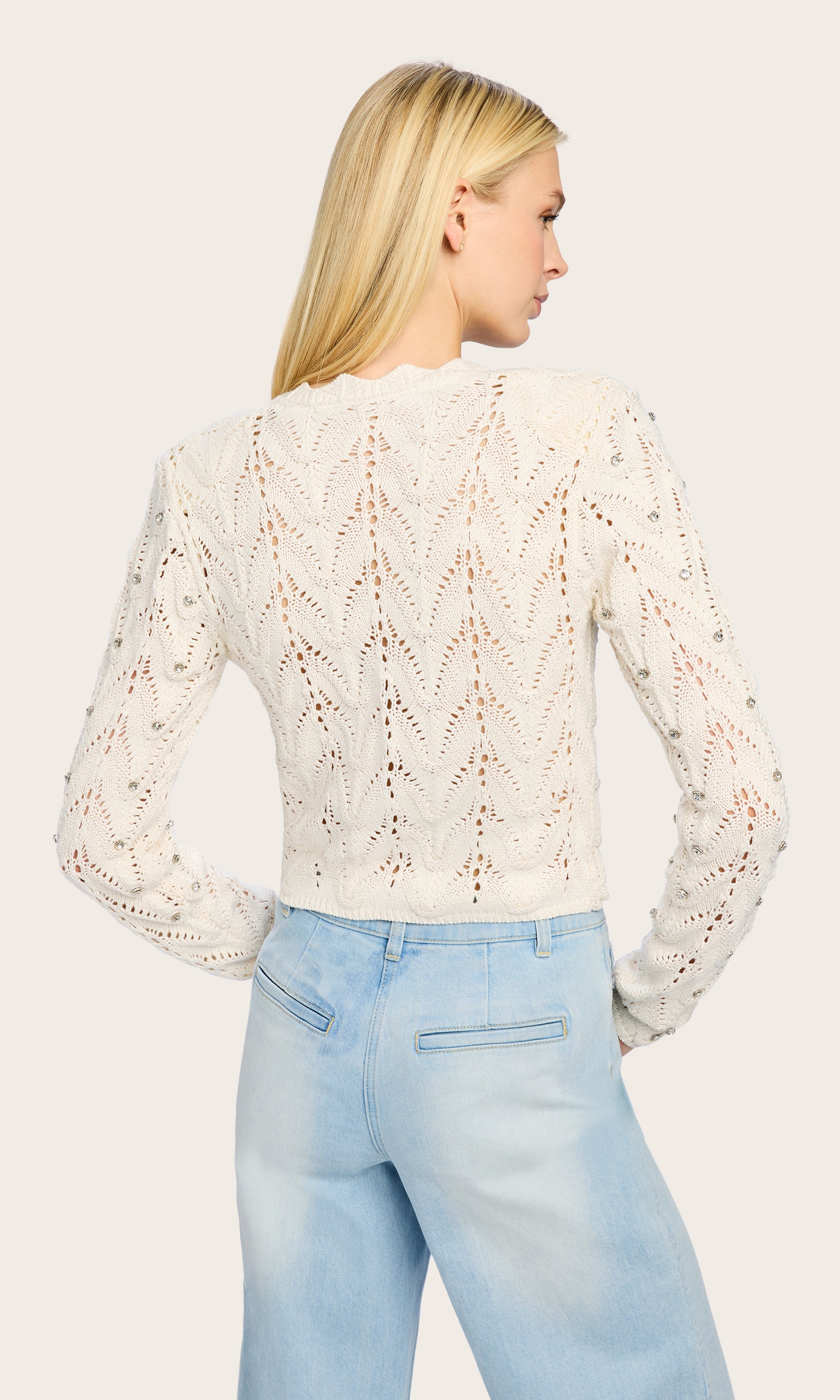 Rear view of the Blake Crystal Pointelle Cardigan worn by the model, offering a glimpse of the scalloped hem and soft silhouette.