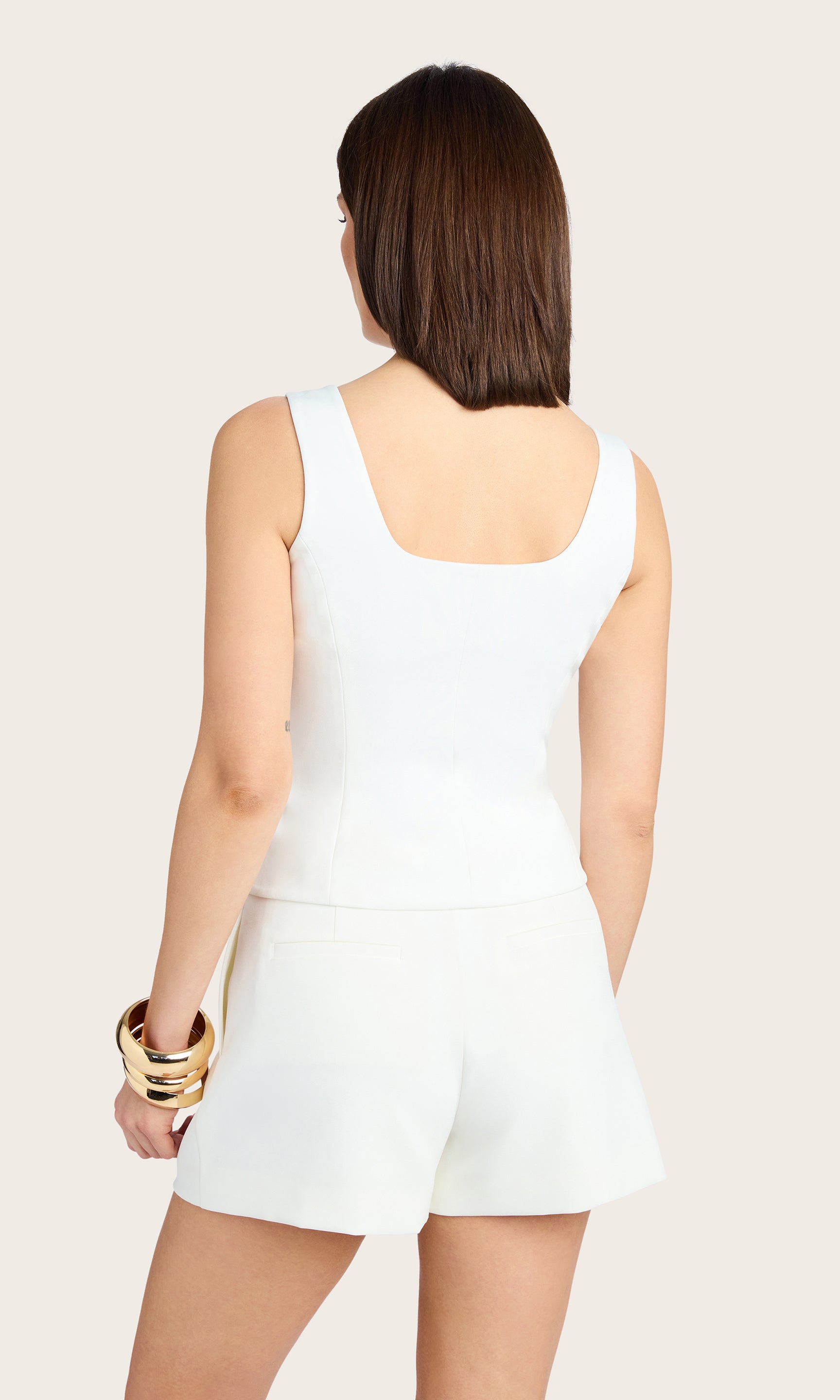 back view of model wearing Beatriz top in white, paired with matching white crepe shorts and accessorized with a gold bracelet and earrings