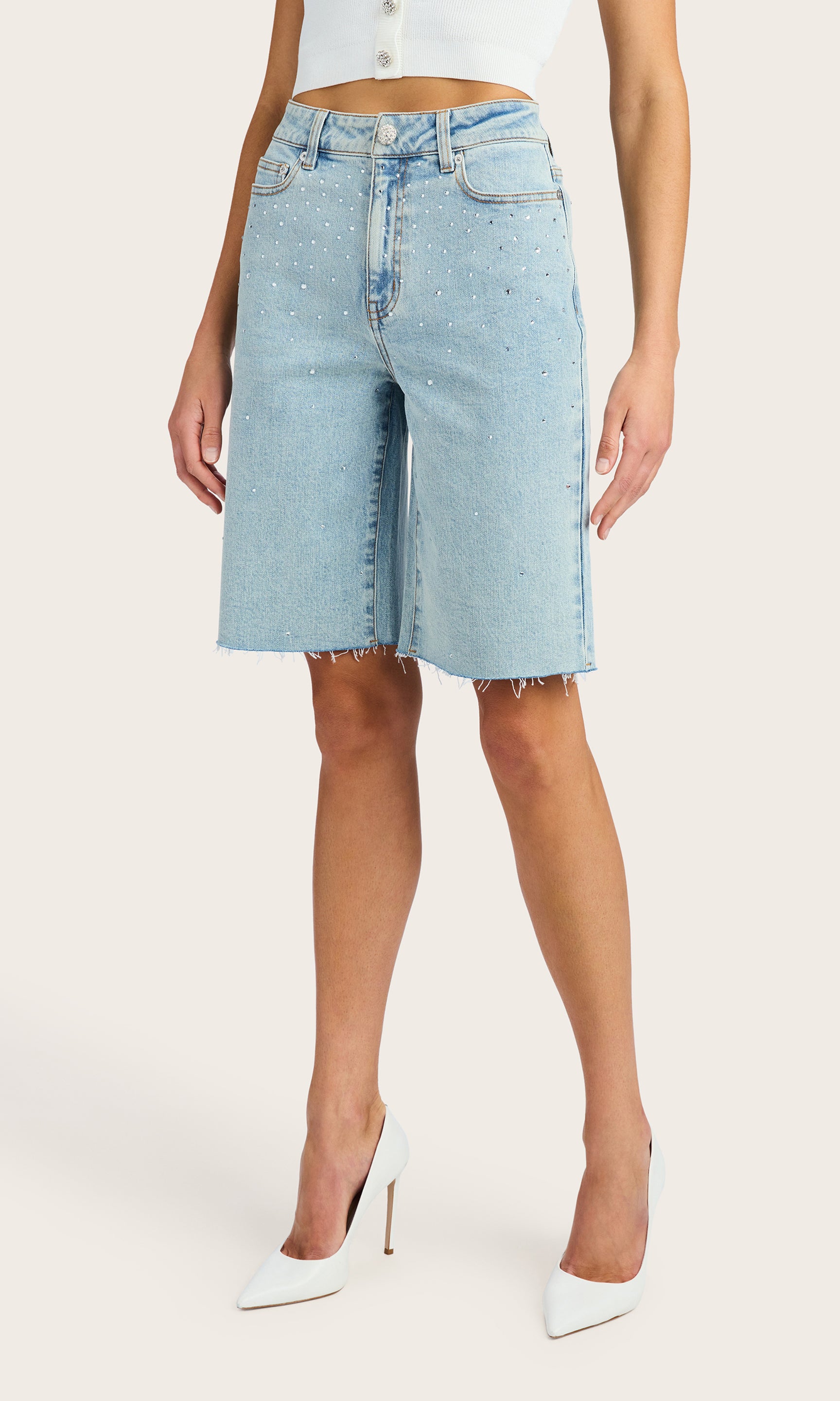 3/4 front view of model wearing the Bellina bermuda shorts in light blue denim adorned with clear crystals, paired with a white tank and white kitten heels
