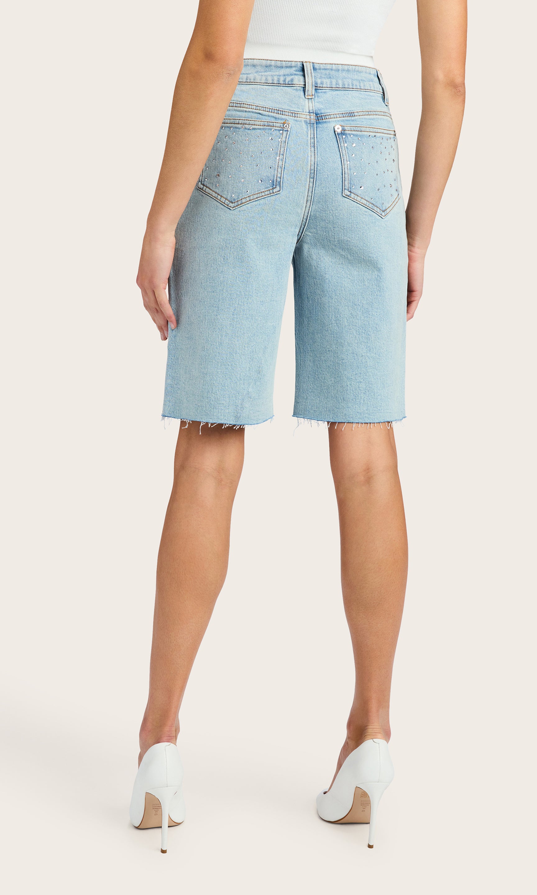 back view of model wearing the Bellina bermuda shorts in light blue denim adorned with clear crystals, paired with a white tank and white kitten heels
