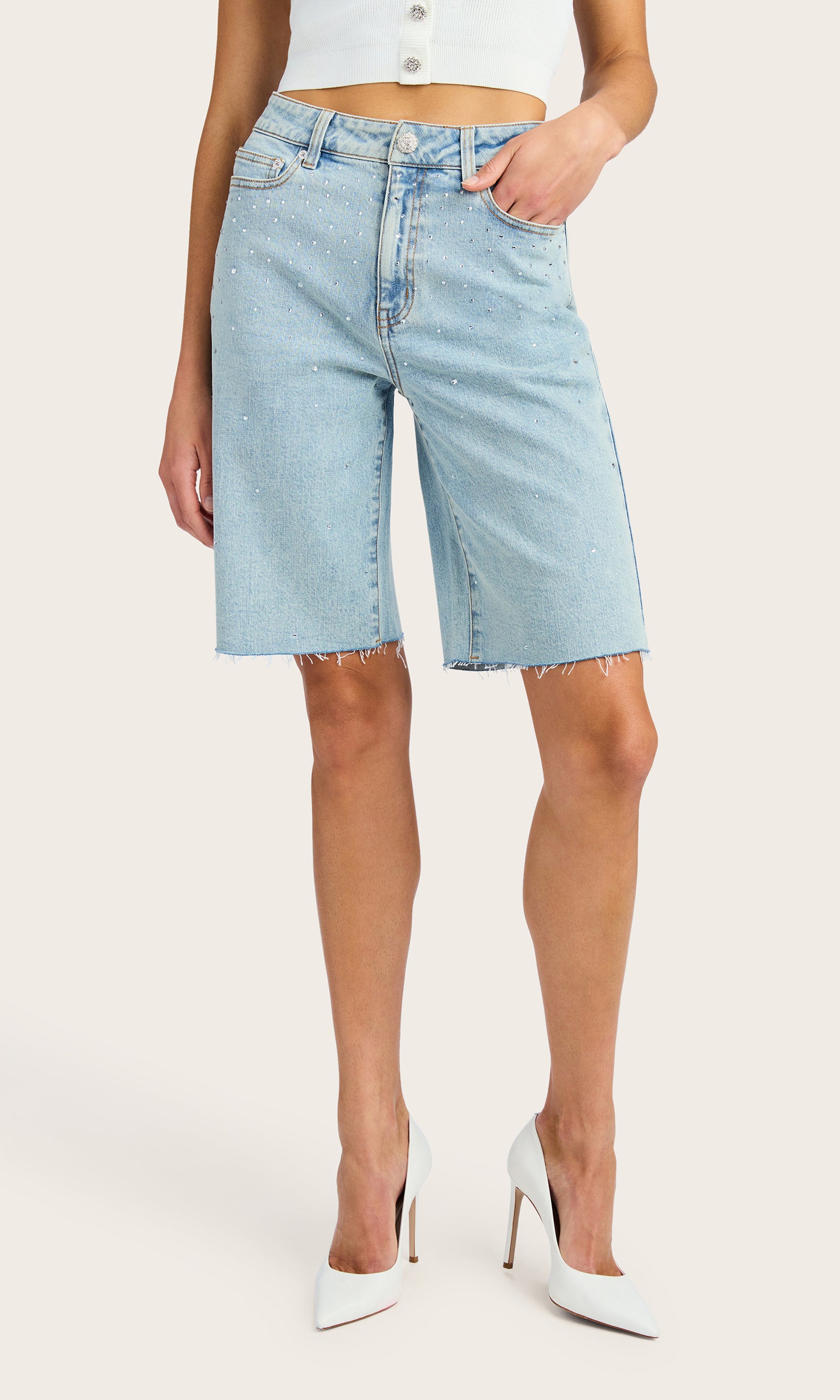 front view of model wearing the Bellina bermuda shorts in light blue denim adorned with clear crystals, paired with a white tank and white kitten heels