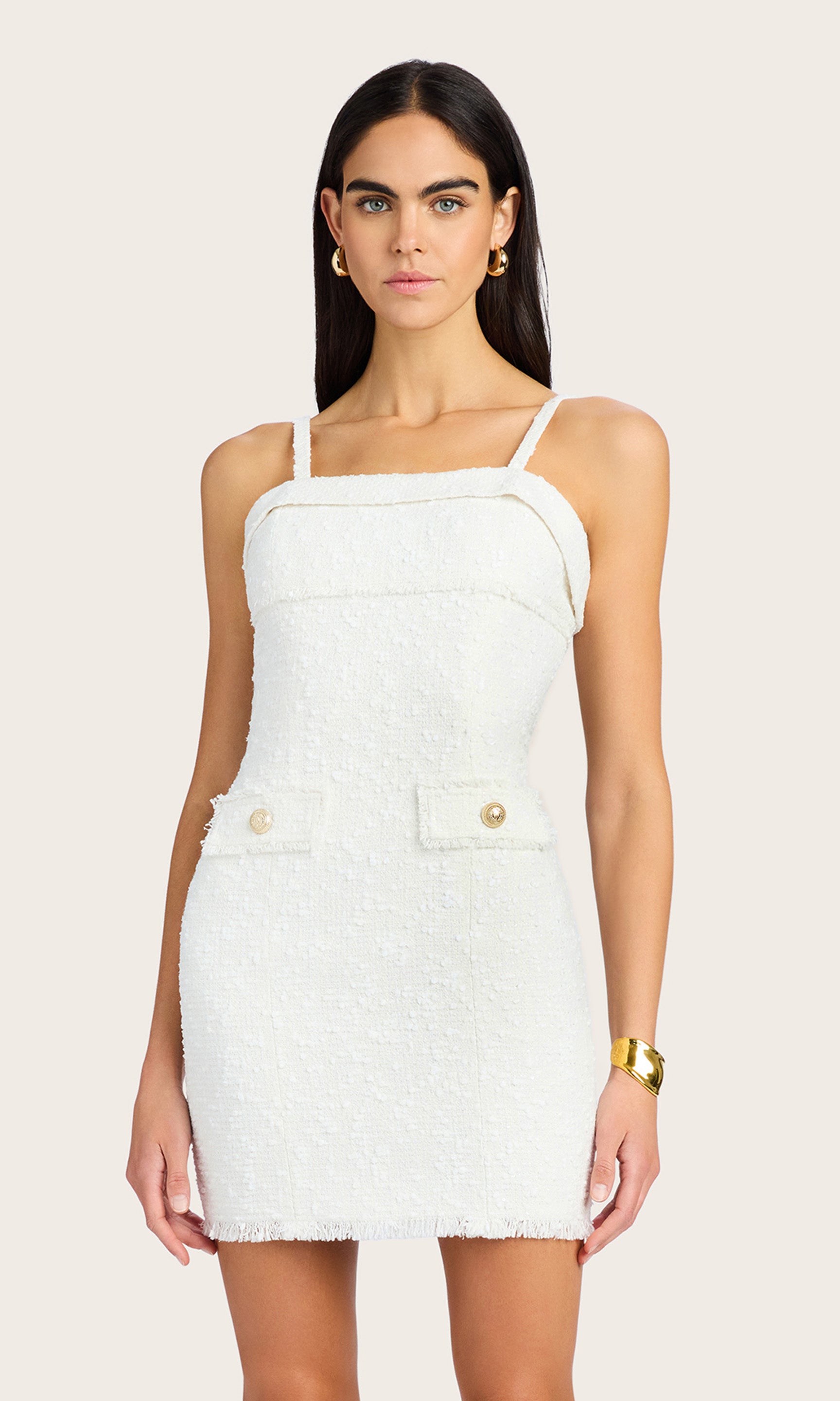 front view of model wearing White Bonnie tweed dress with faux pockets embellished with gold ripple buttons, accessorized with gold earrings and a gold bracelet