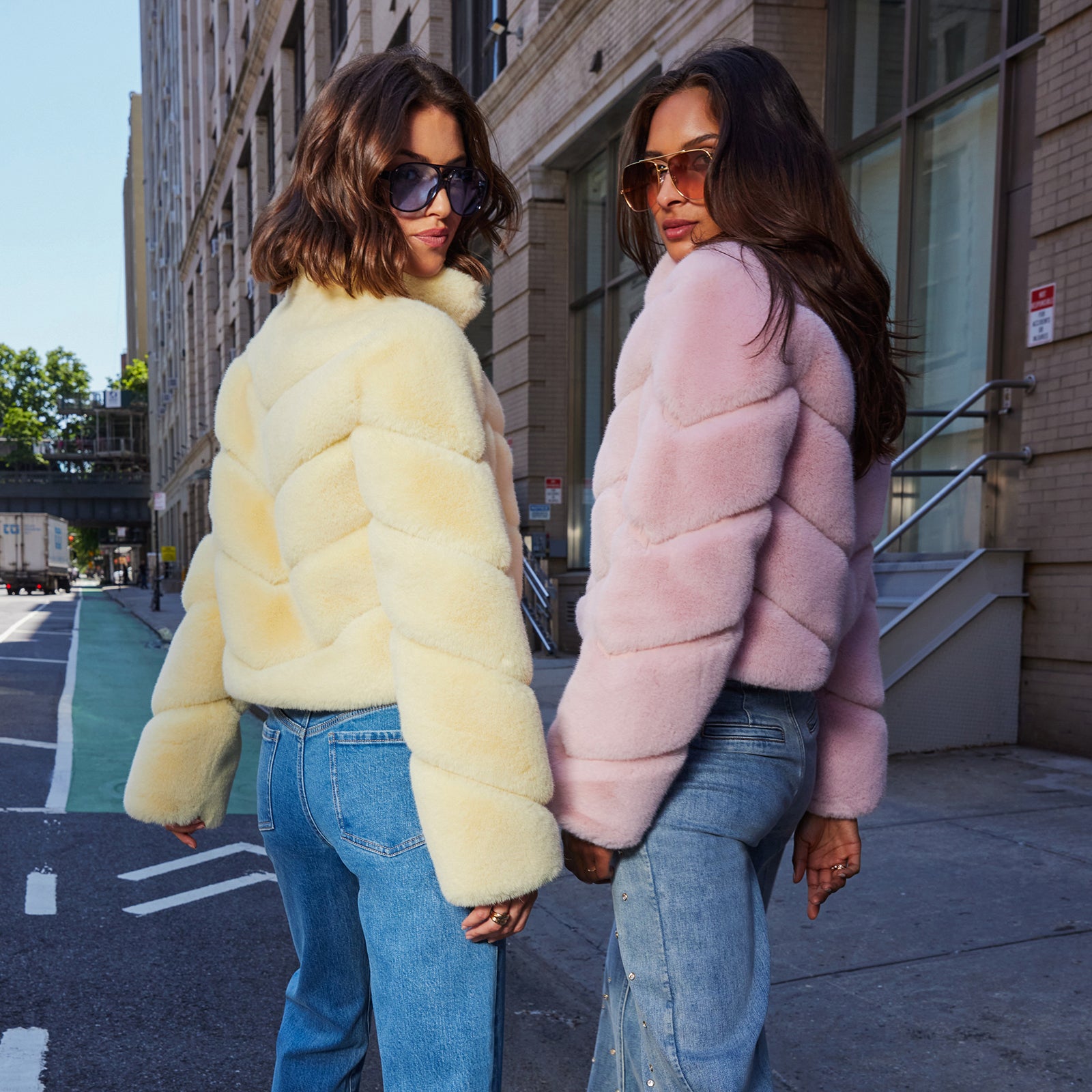 Two women wearing pastel colored faux fur jackets on a city street.