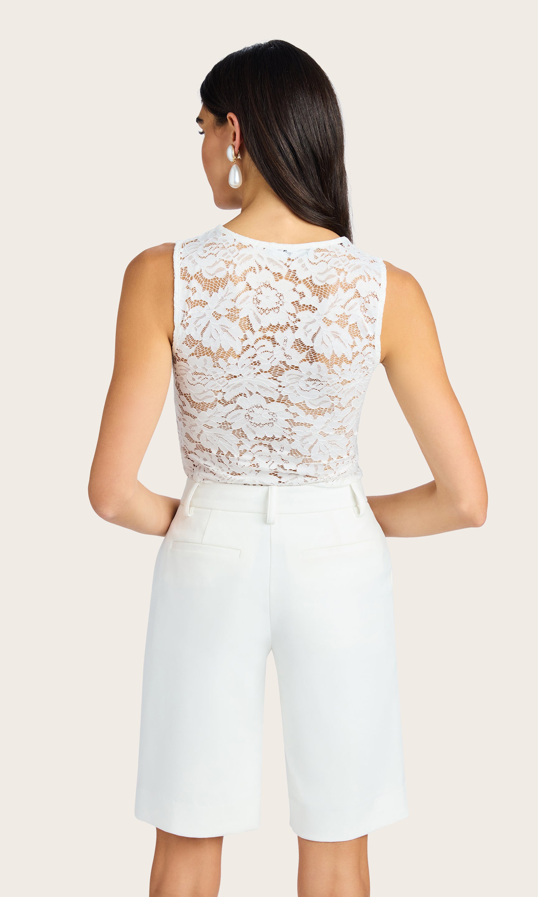 back view image of model wearing the Brinley lace tank in white with petite pearl buttons down the front, paired with white bermuda shorts and accessorized with big pearl rain drop earrings