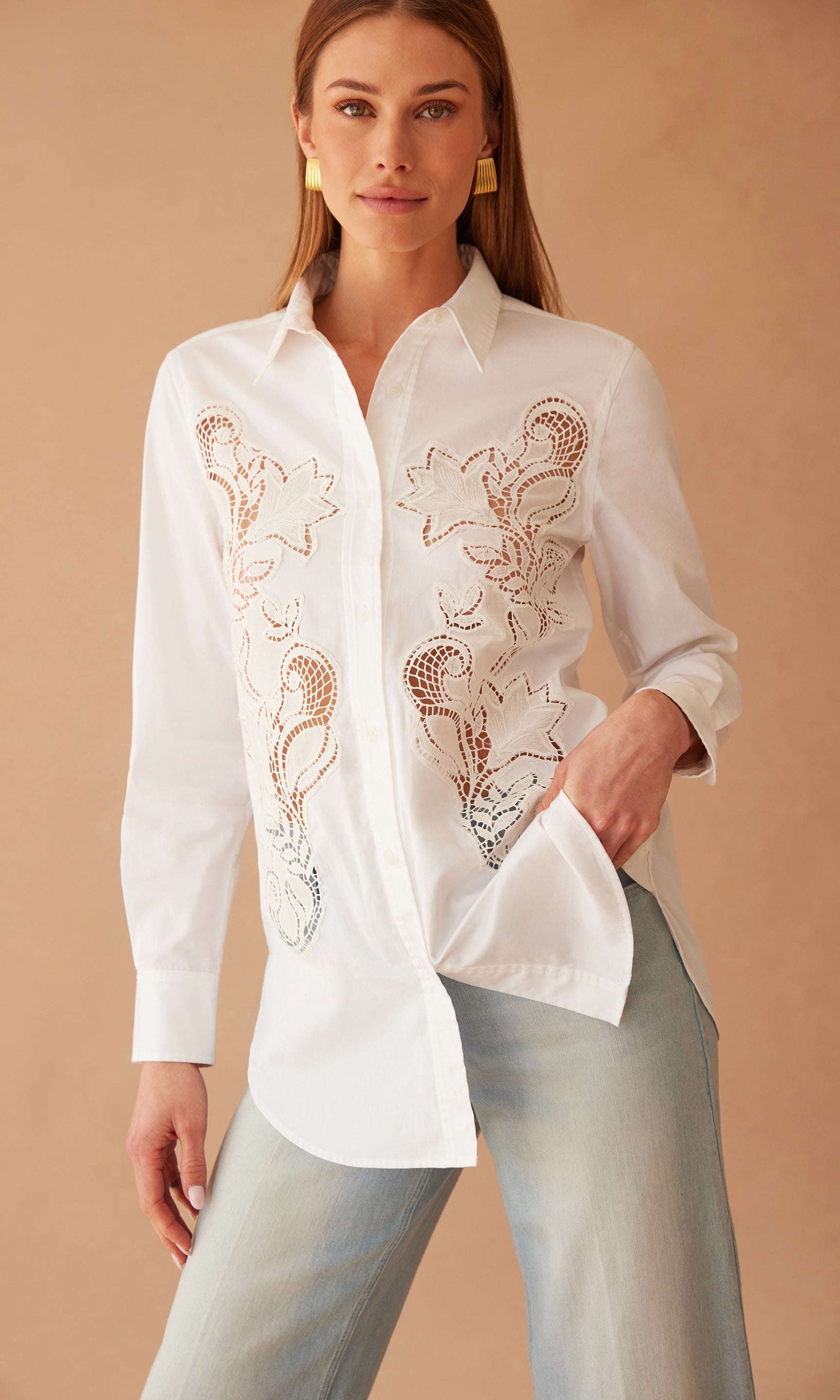 image of model in front of a sandy peach wall wearing the white Bruno button down shirt in white paired with blue jeans