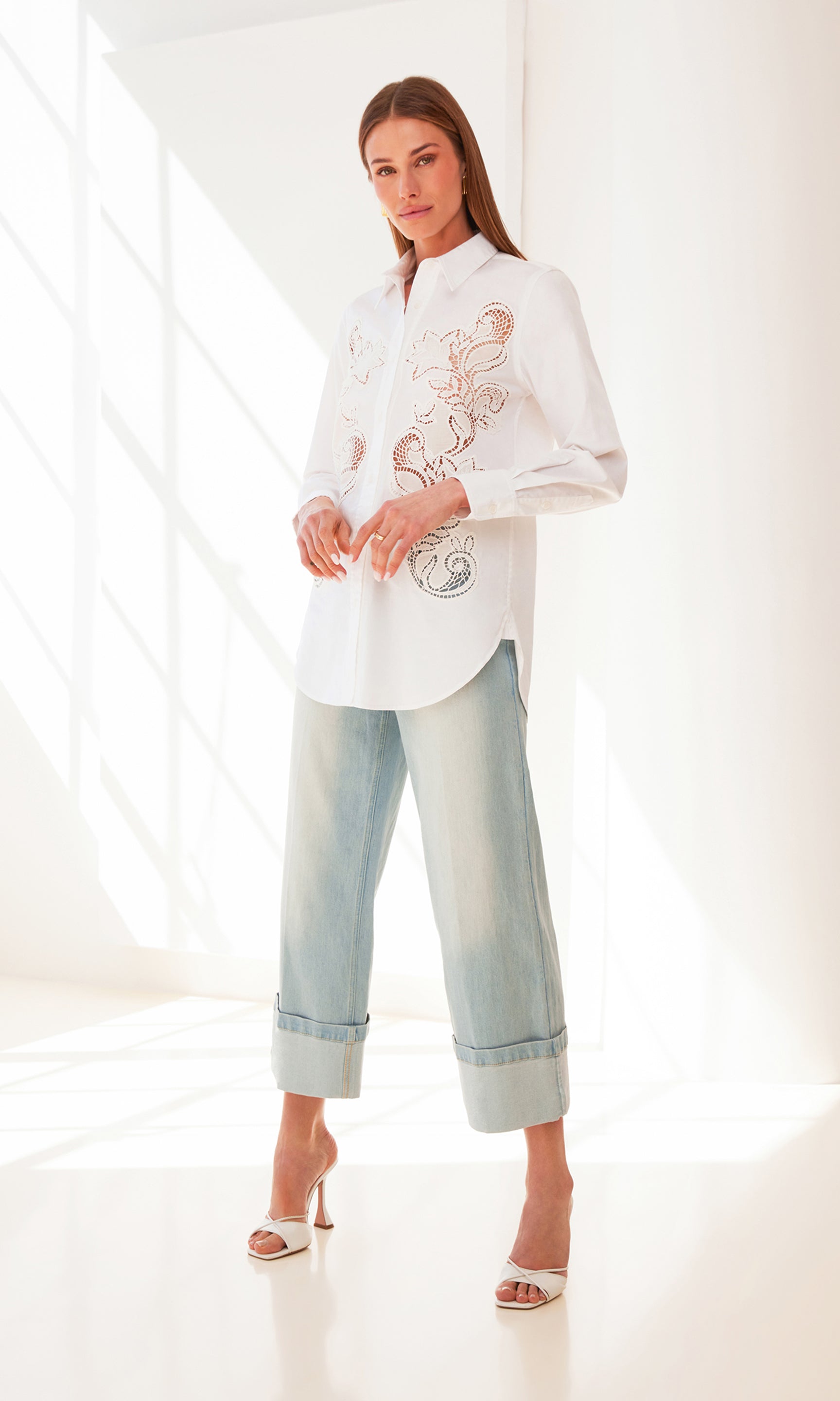image of model inside a white room near a window wearing the white Bruno button down shirt in white paired with blue jeans and white heels