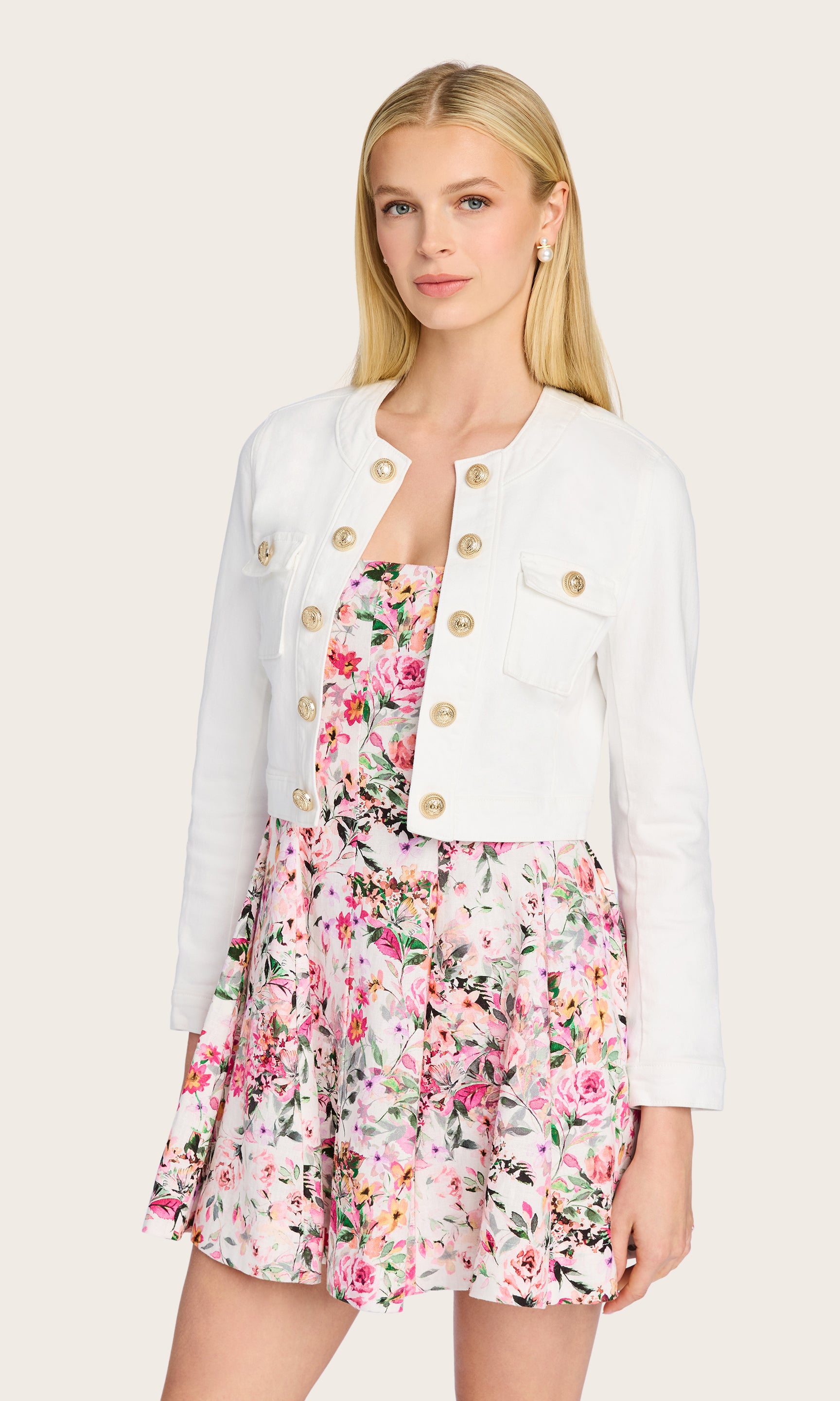 The model wears the Valentina Denim Jacket in a front-facing pose, styled with a floral mini dress to highlight the jacket's crisp structure and gold buttons.
