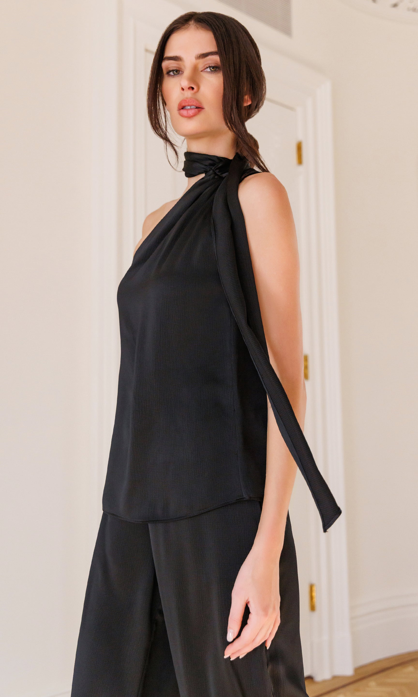 Woman wearing a black sleeveless top with a halter neck design in an indoor setting.