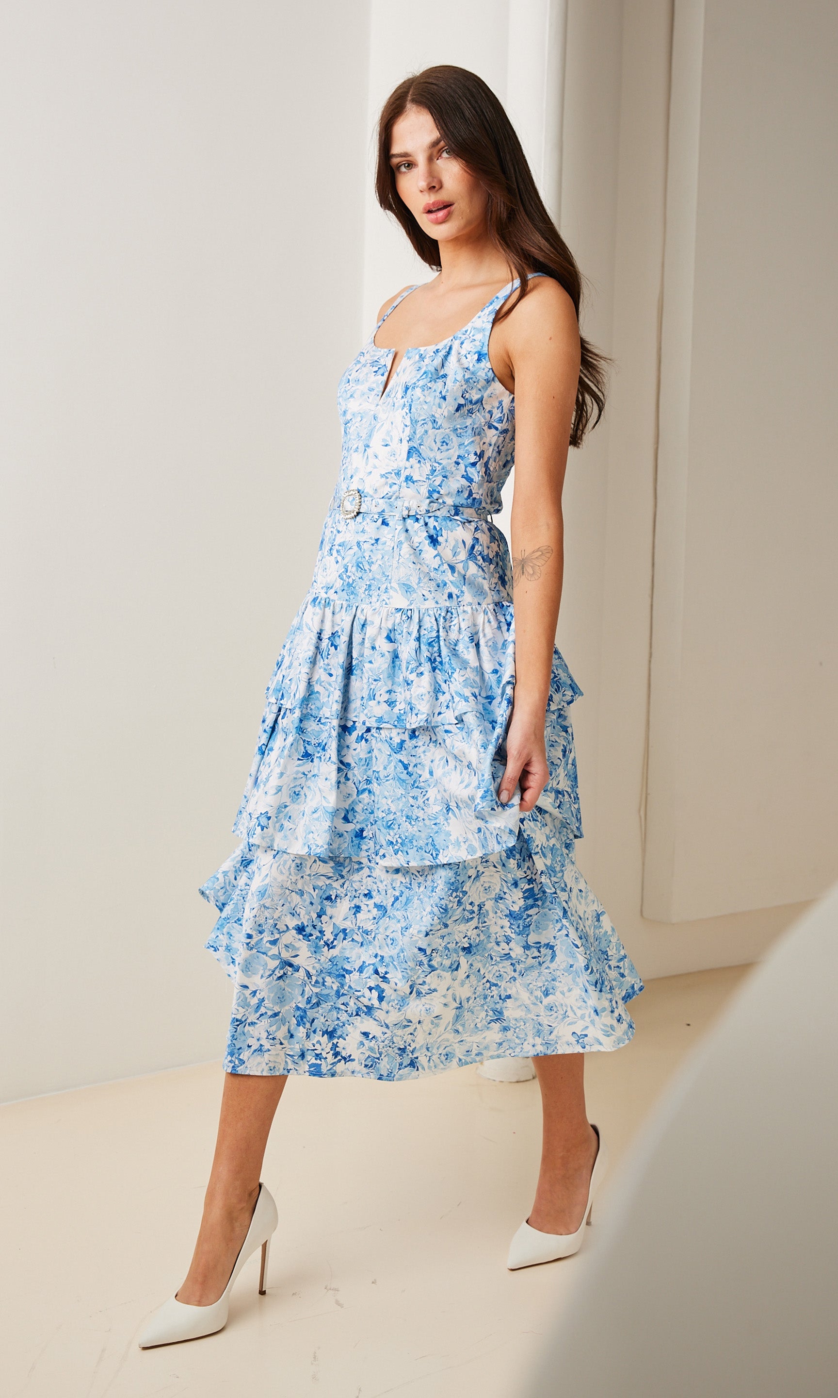 Indoor Image Of Model Wearing A Blue Floral Midi Dress, Standing Against A Neutral Backdrop
