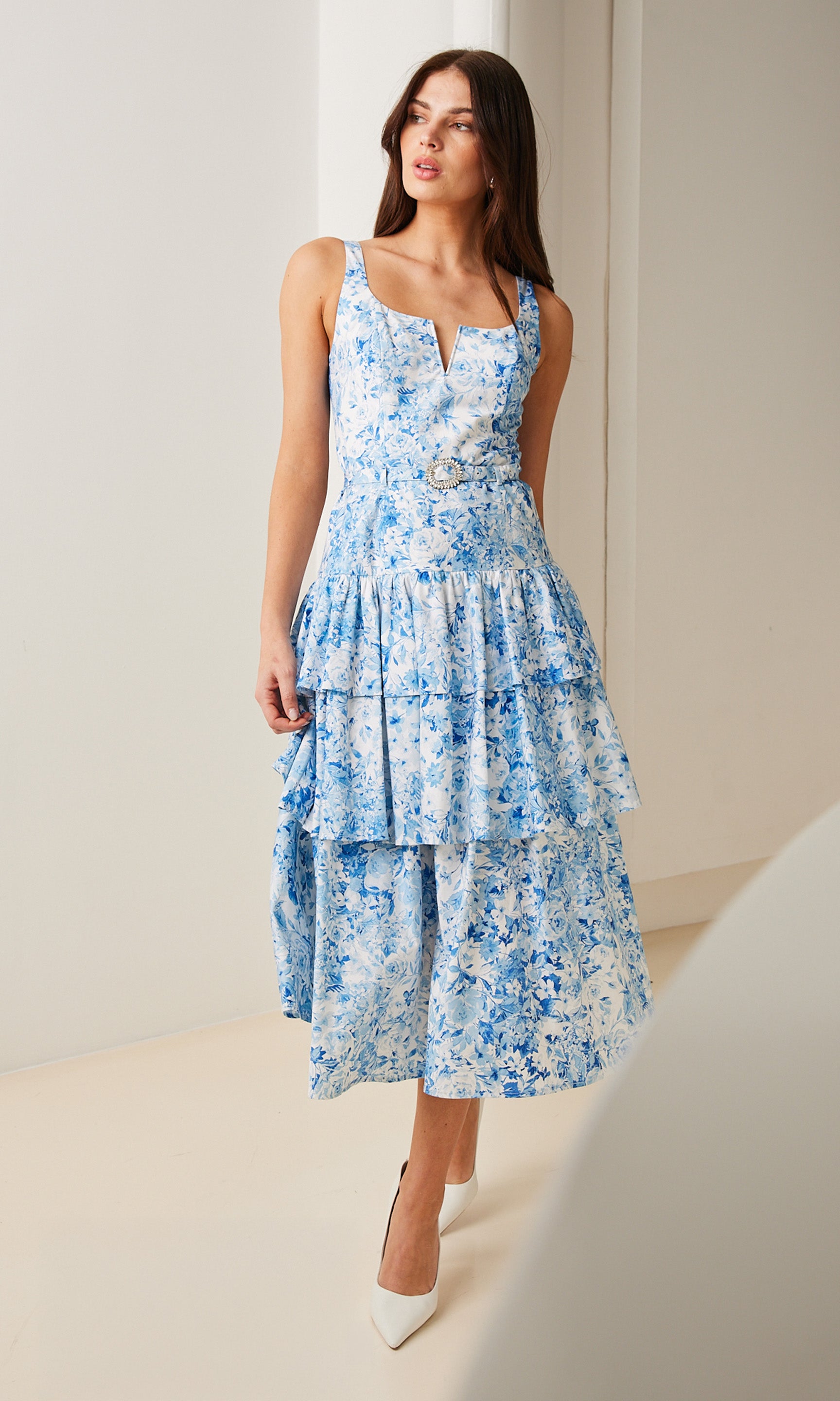 Image of Model Wearing A Blue Floral Midi Dress paired white kitten heels; indoors in a white softly lit room