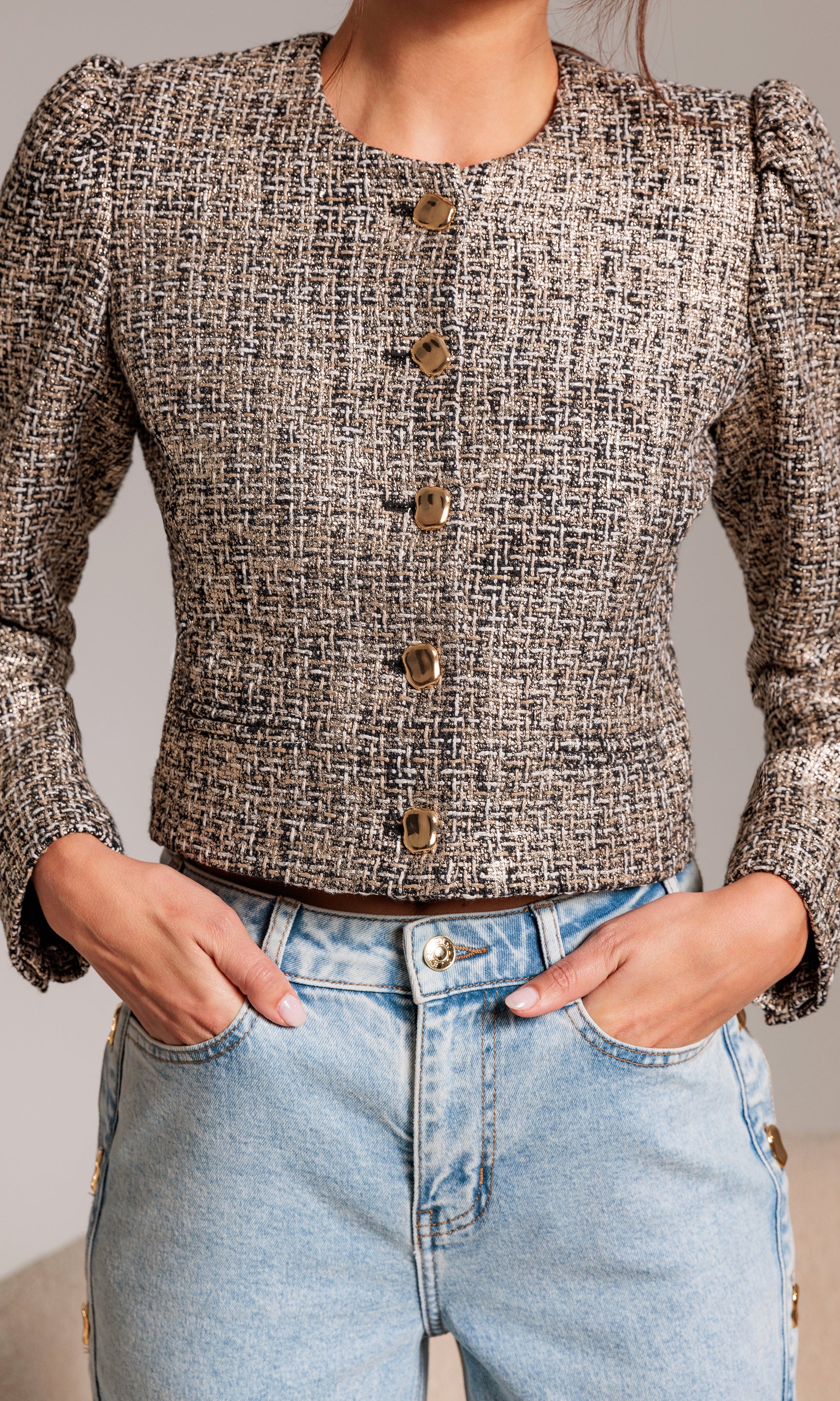 Person wearing a tweed jacket and light blue jeans against a neutral background