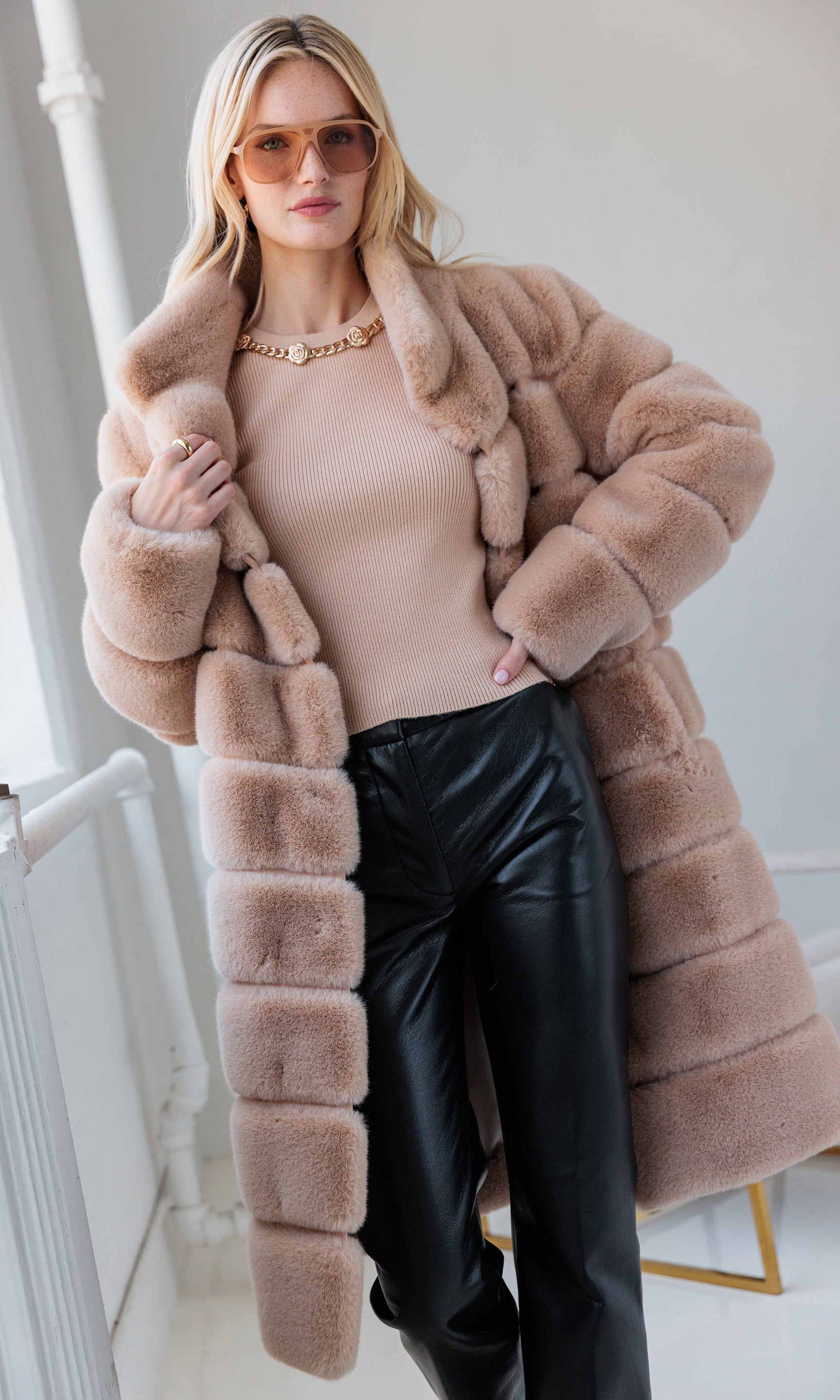 Woman wearing a long beige fur coat with a plain background