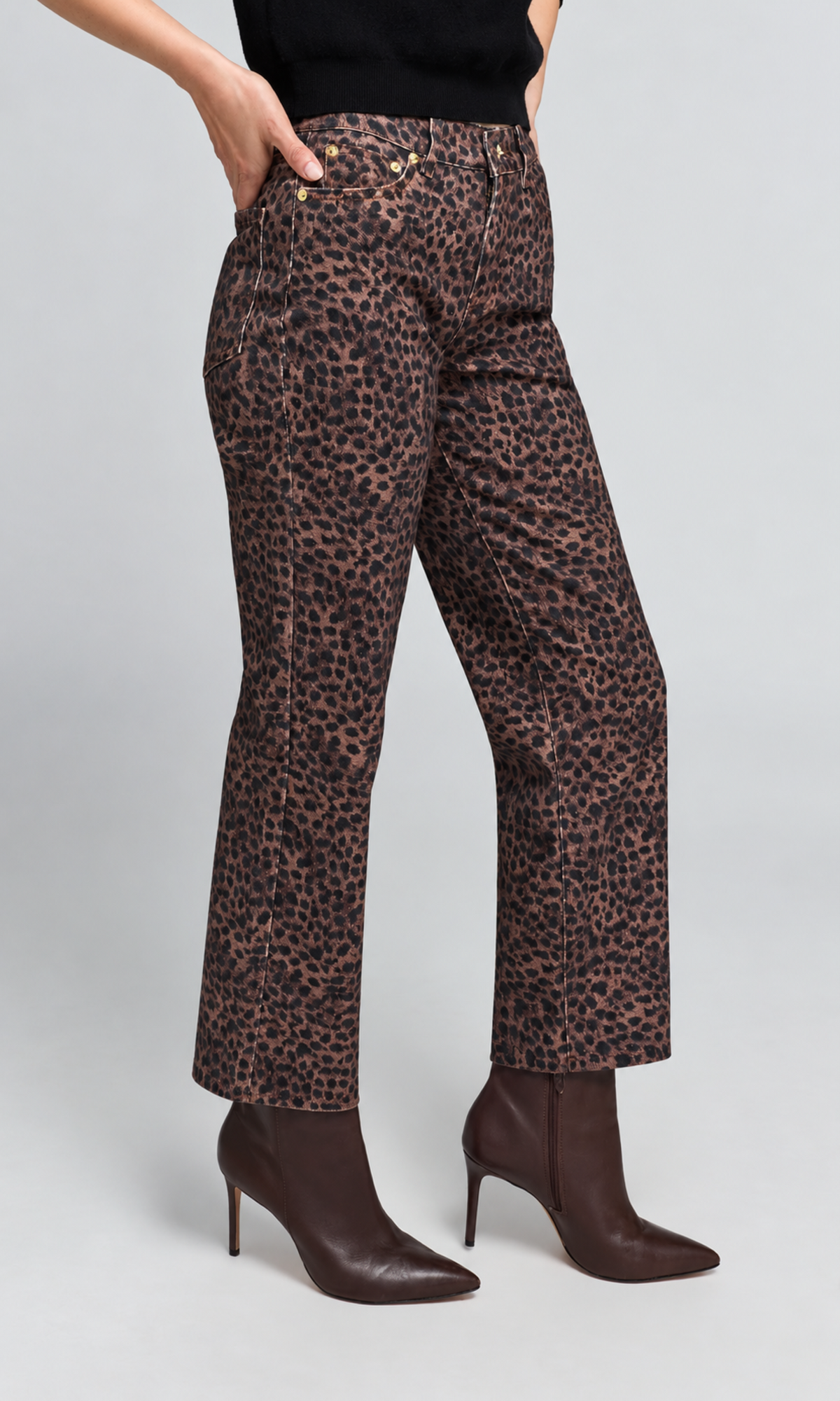 A model from the waist down wearing brown leopard-print cropped pants, a black top, and dark brown heeled ankle boots, set against a light gray studio background.