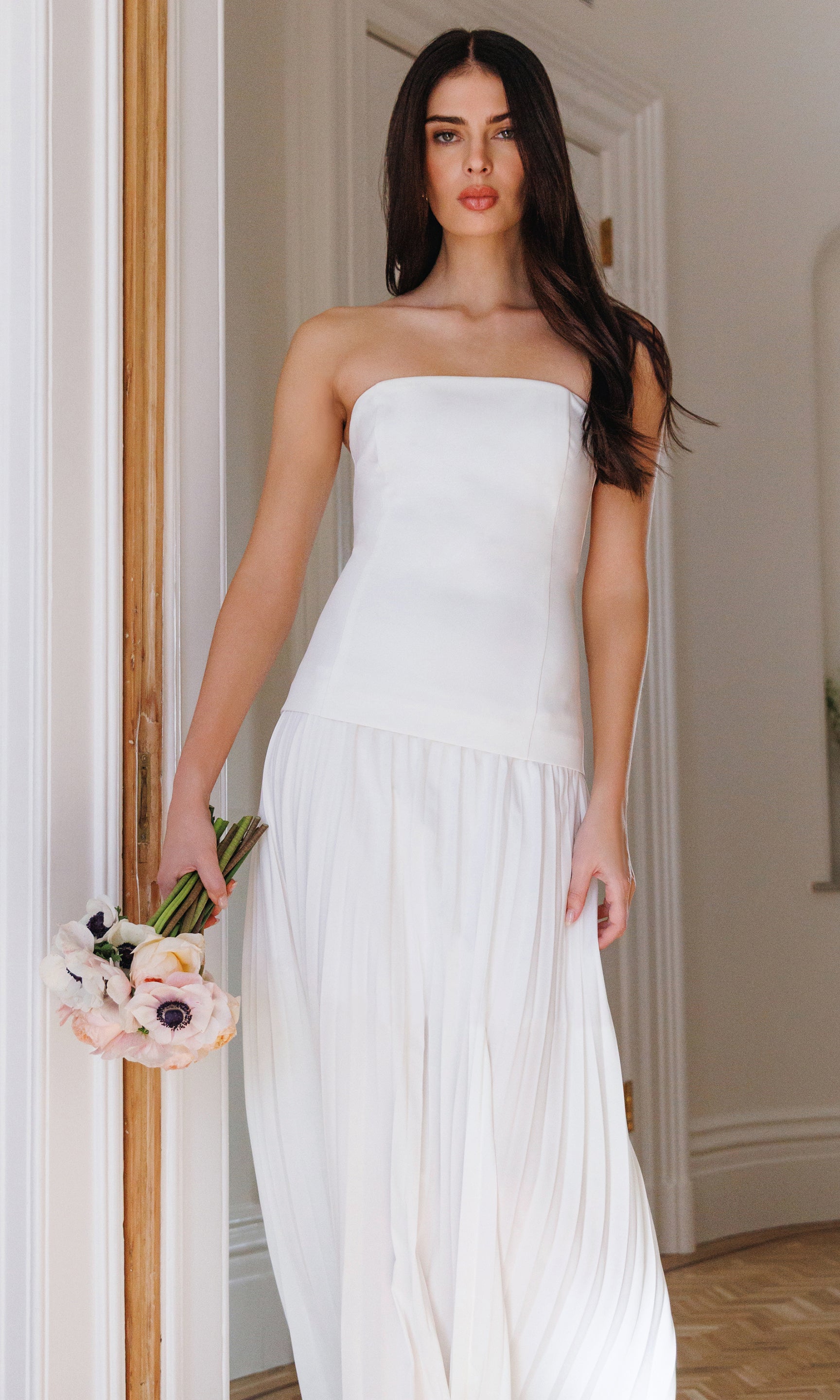 Woman in a white strapless dress holding flowers indoors.