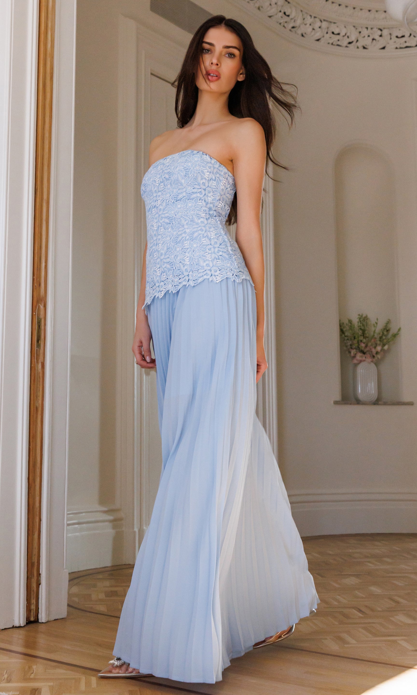 Woman wearing a light blue strapless dress with a textured bodice and flowing skirt in an elegant room.