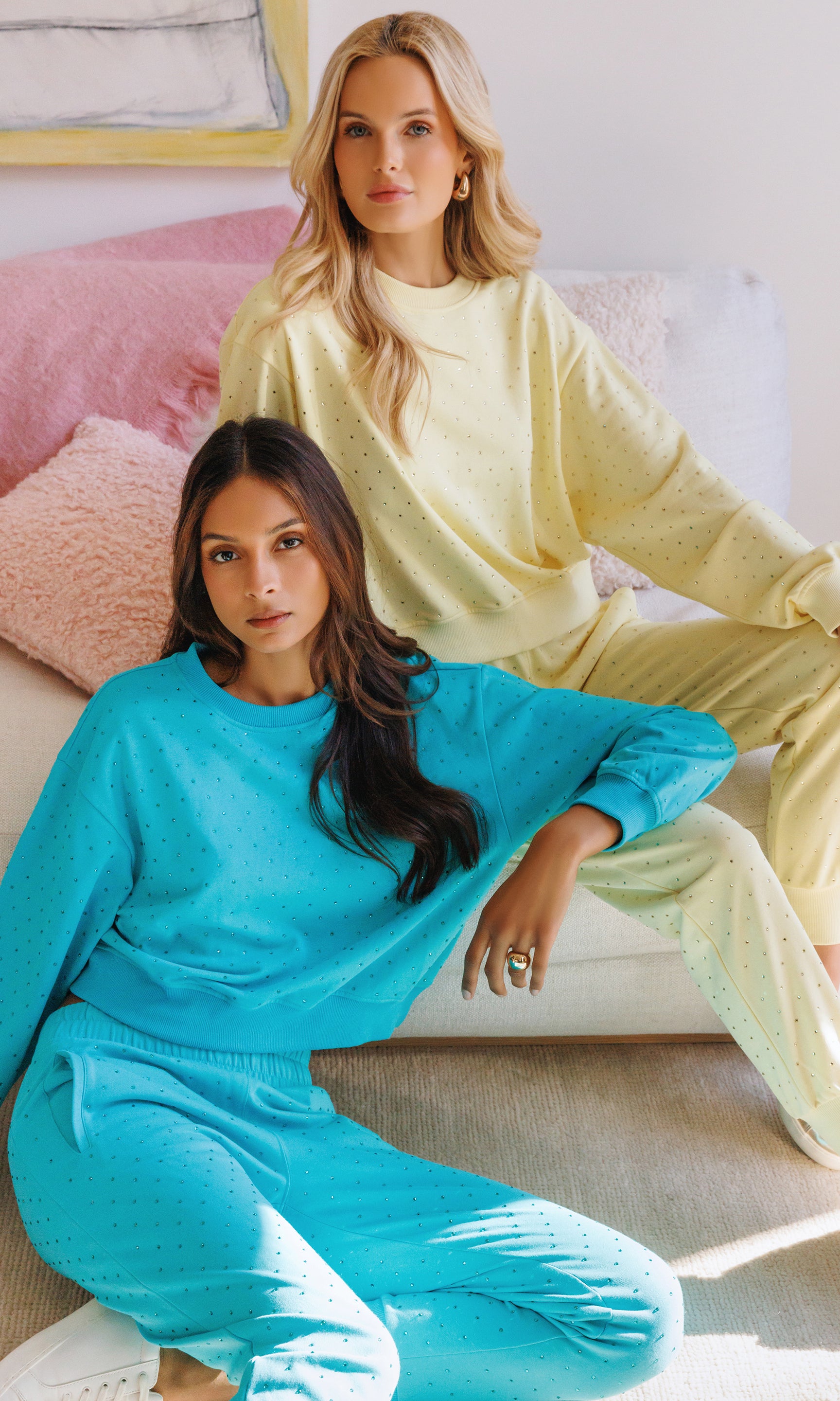 Two women wearing matching teal and yellow outfits sitting on a couch.