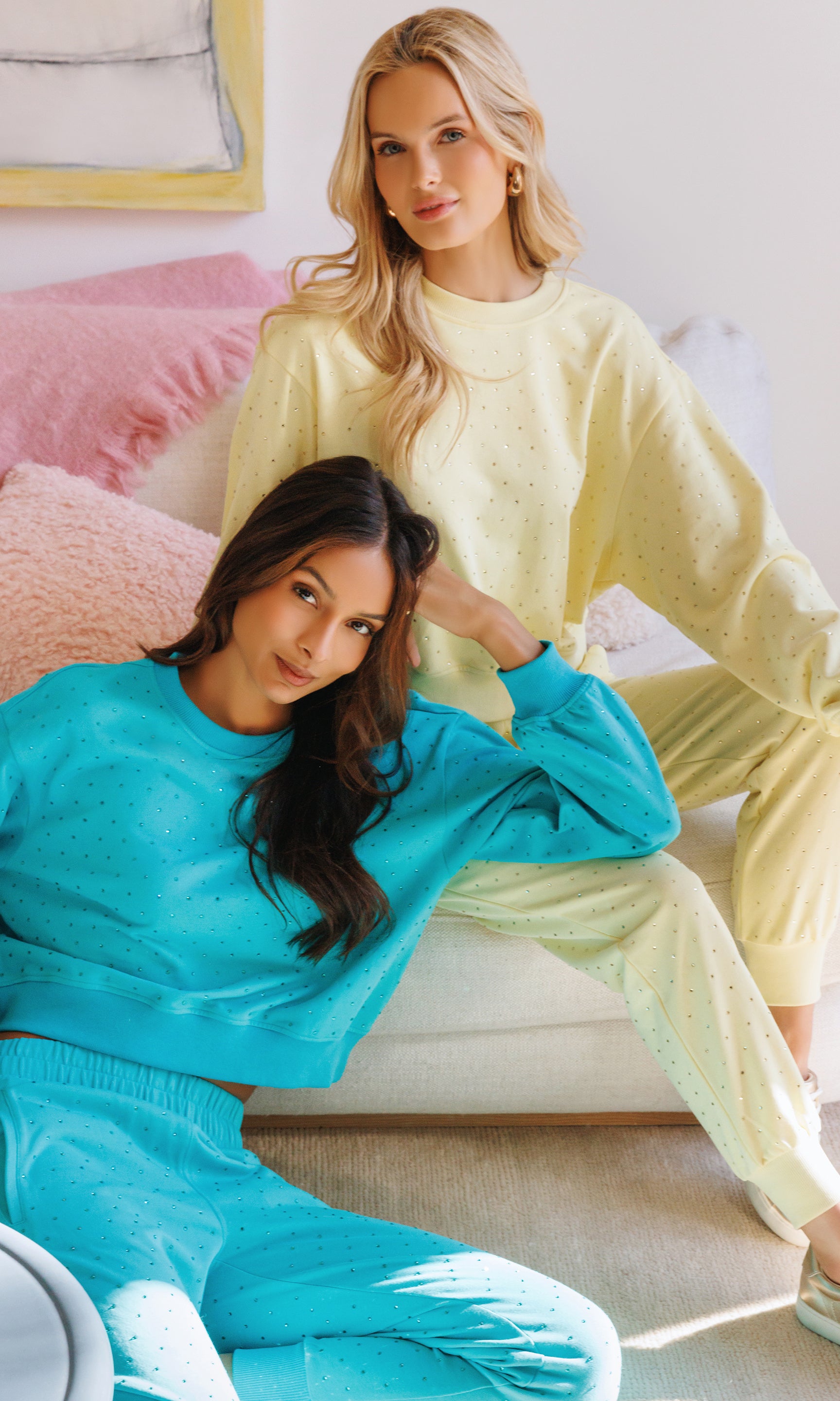 Two women sitting on a couch, one in a yellow outfit and the other in a blue outfit.