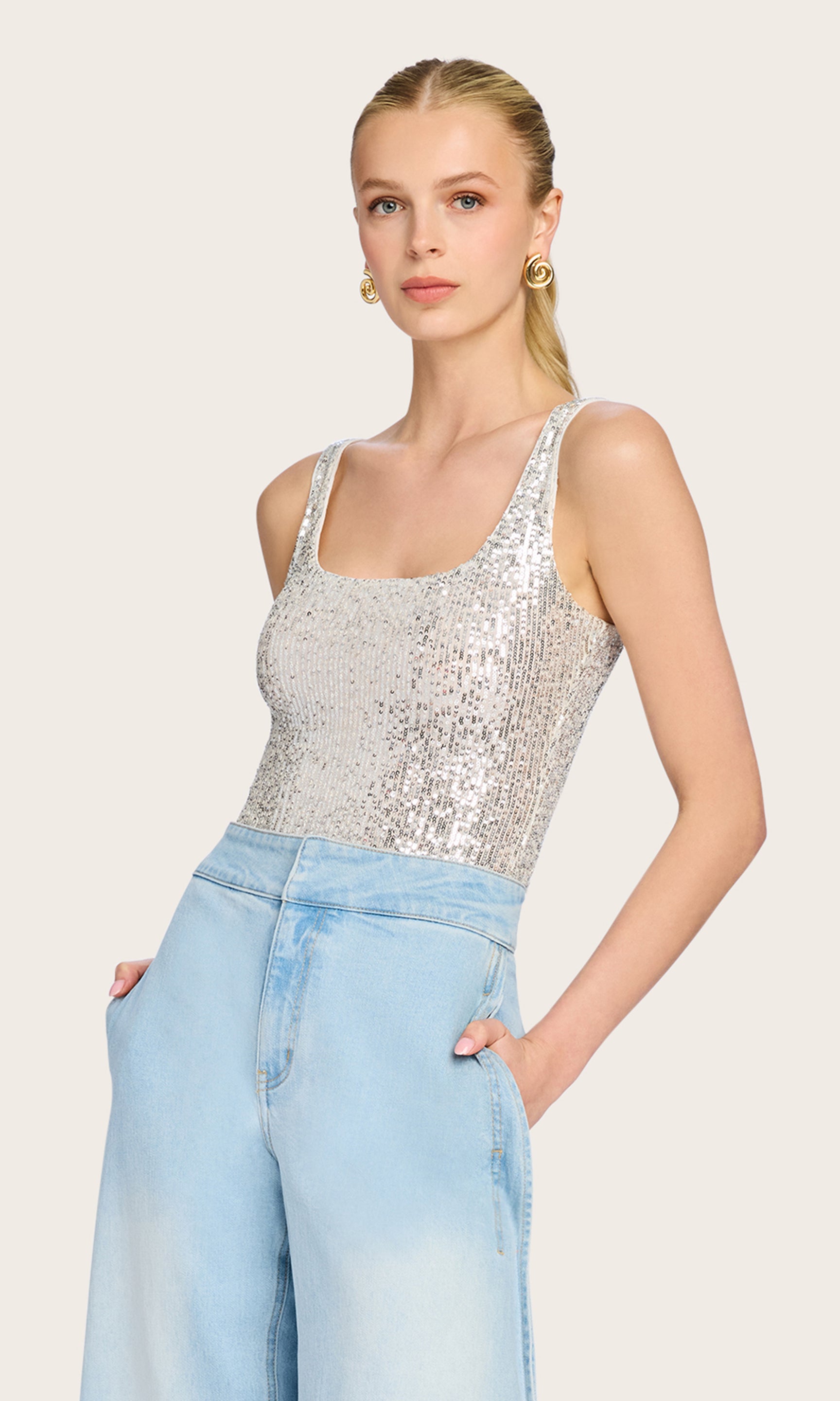 Front view of the model wearing the Dina Sequin Bodysuit in silver sequins paired with light-wash denim for a laid-back glam vibe.