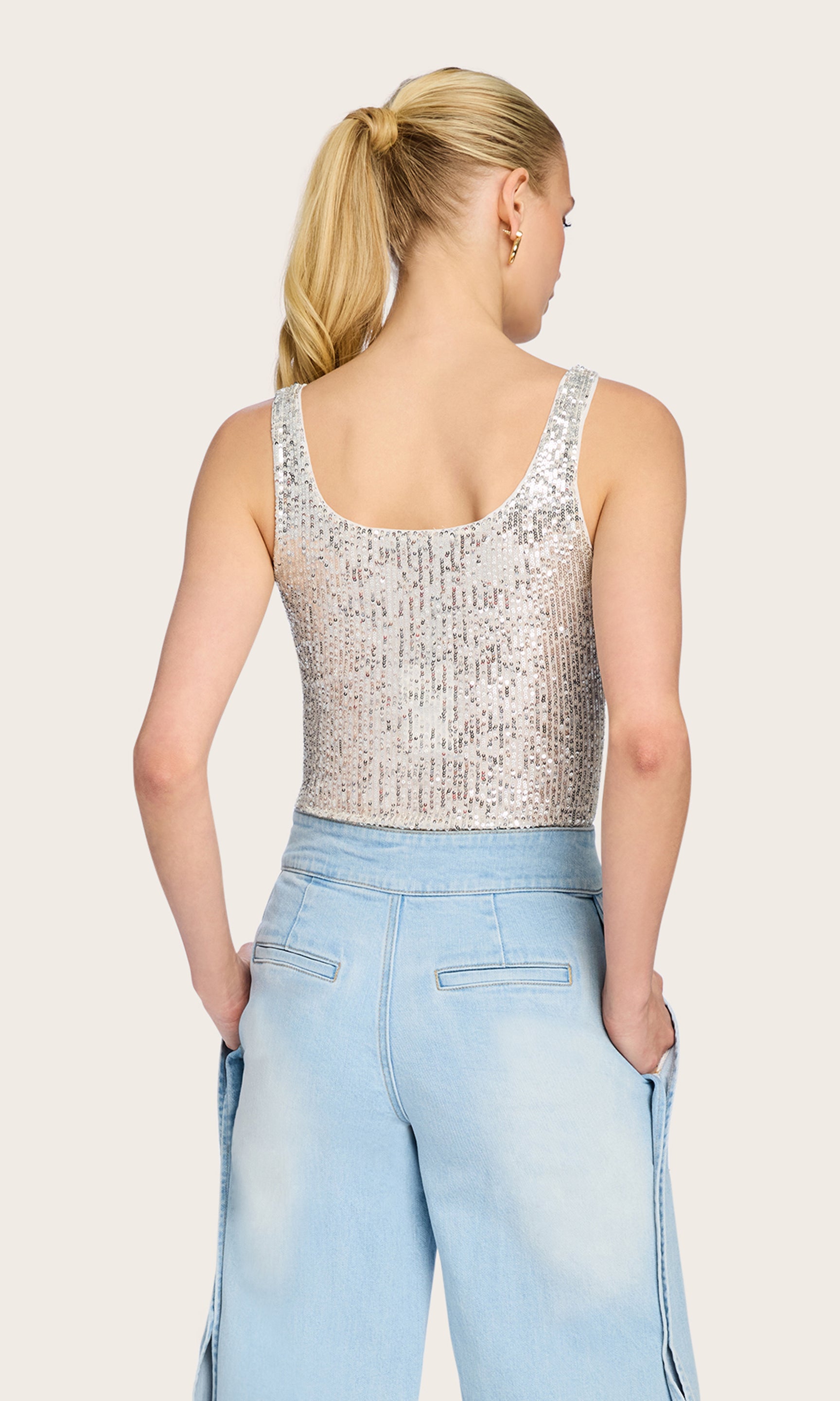 Rear view of the model in the Dina Sequin Bodysuit in silver sequins styled with denim, showing the open-back cut and flattering shape.