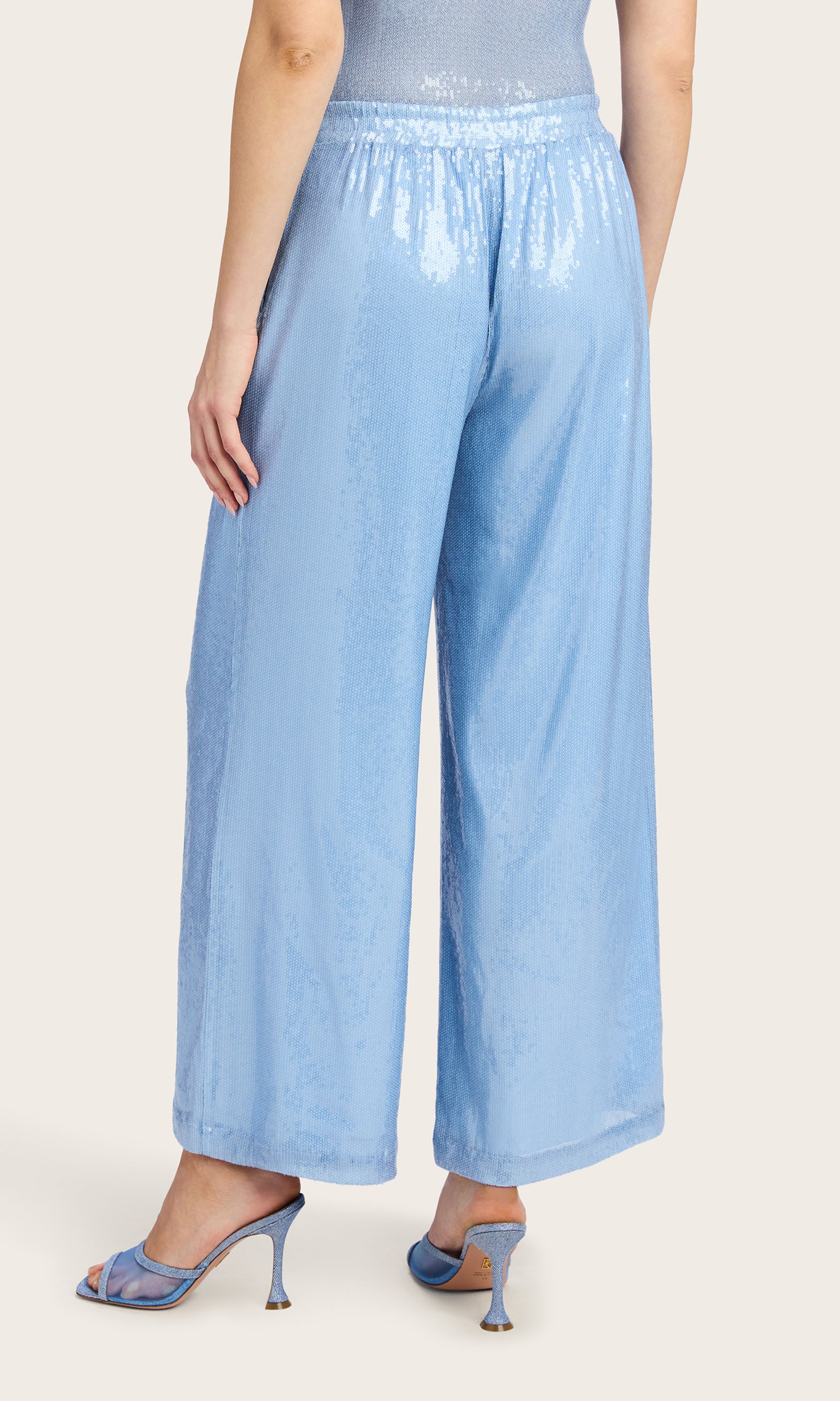 Back view image of the model wearing the Talia Sequin Pants in light blue, styled with a matching sleeveless bodysuit and heels.