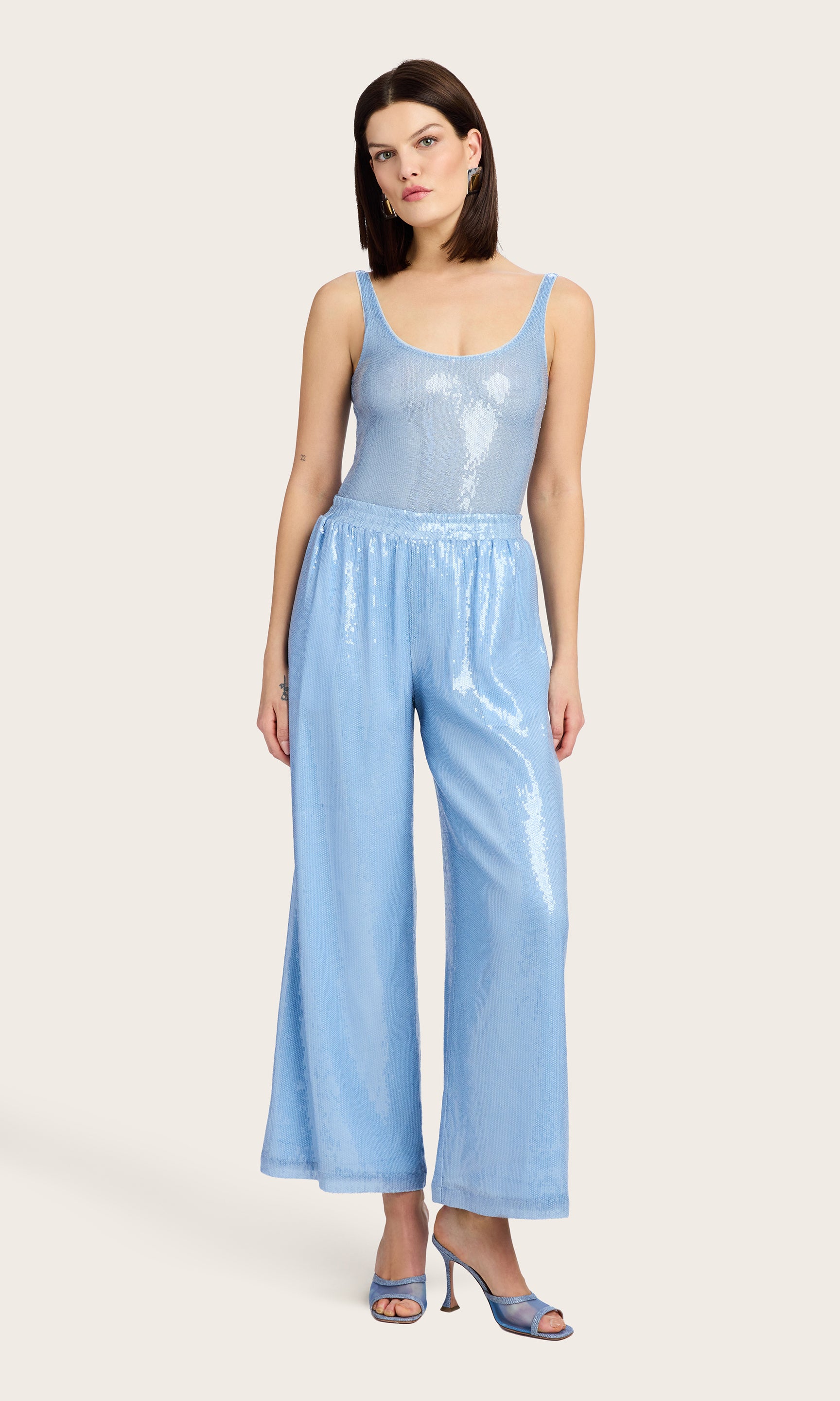 Full body image of the model wearing the Talia Sequin Pants in light blue, styled with a matching sleeveless bodysuit and heels.