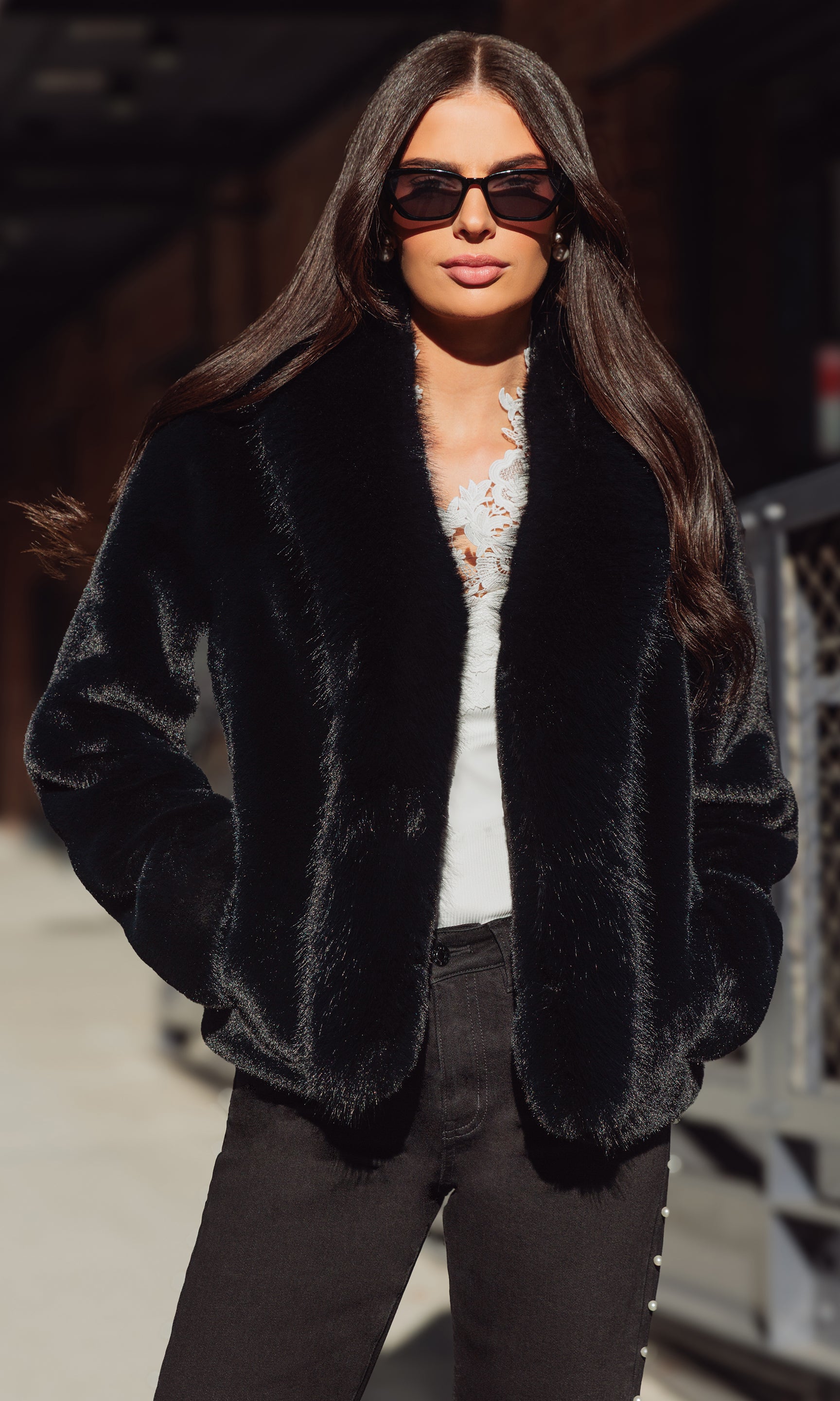 Woman wearing a black fur coat and sunglasses outdoors.