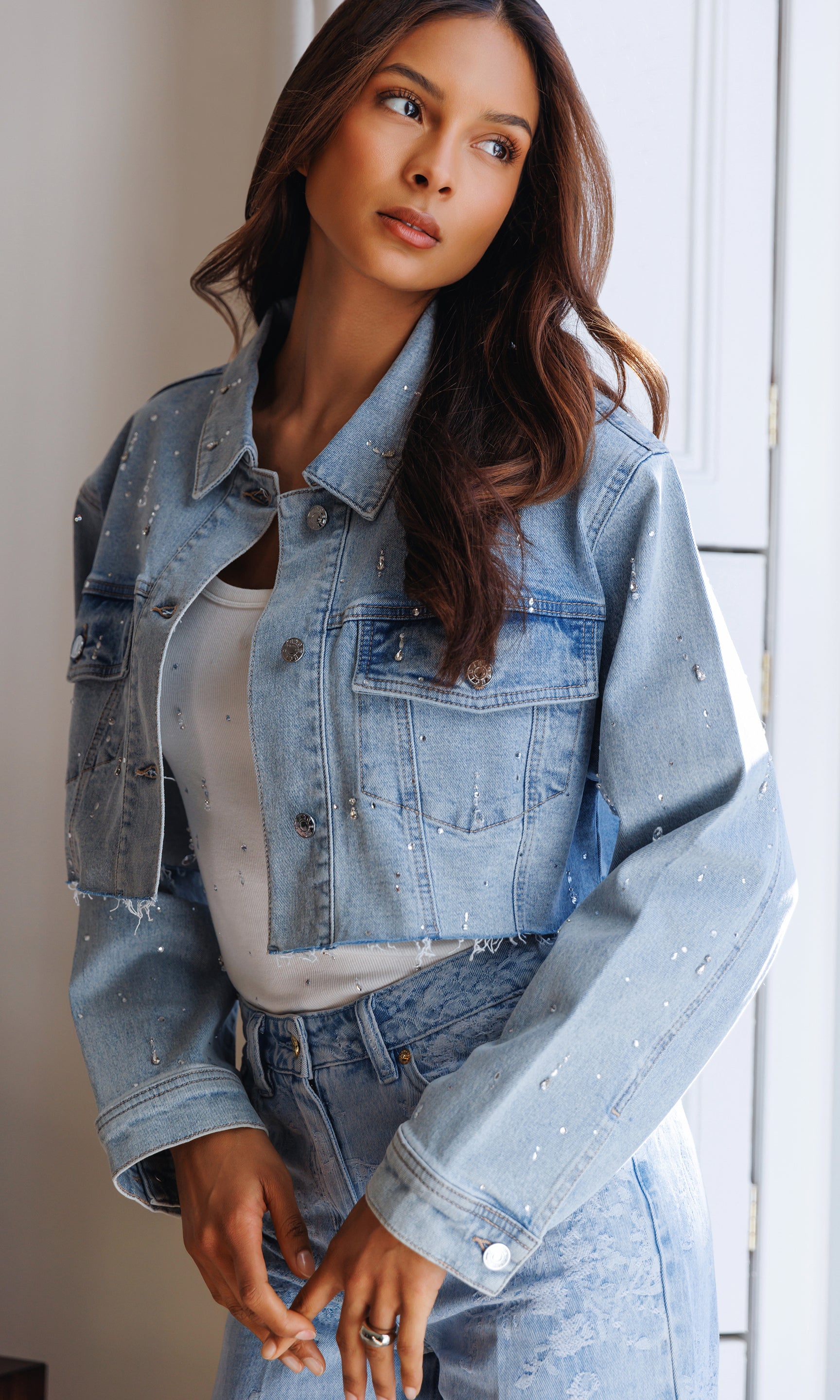 Woman wearing a light blue denim jacket with crystal embellishments and jeans indoors.