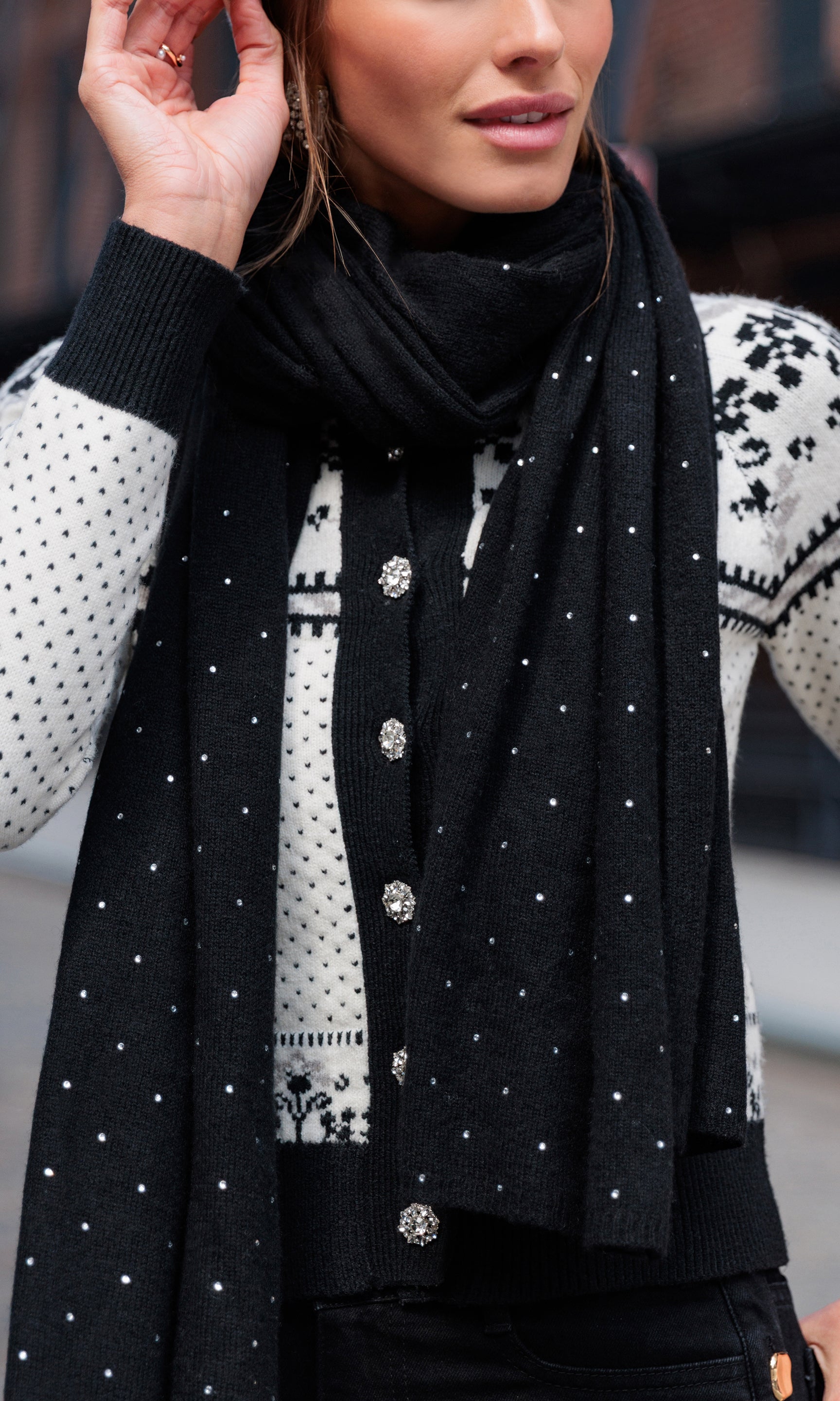 Woman wearing a black scarf with white crystals over a patterned sweater.