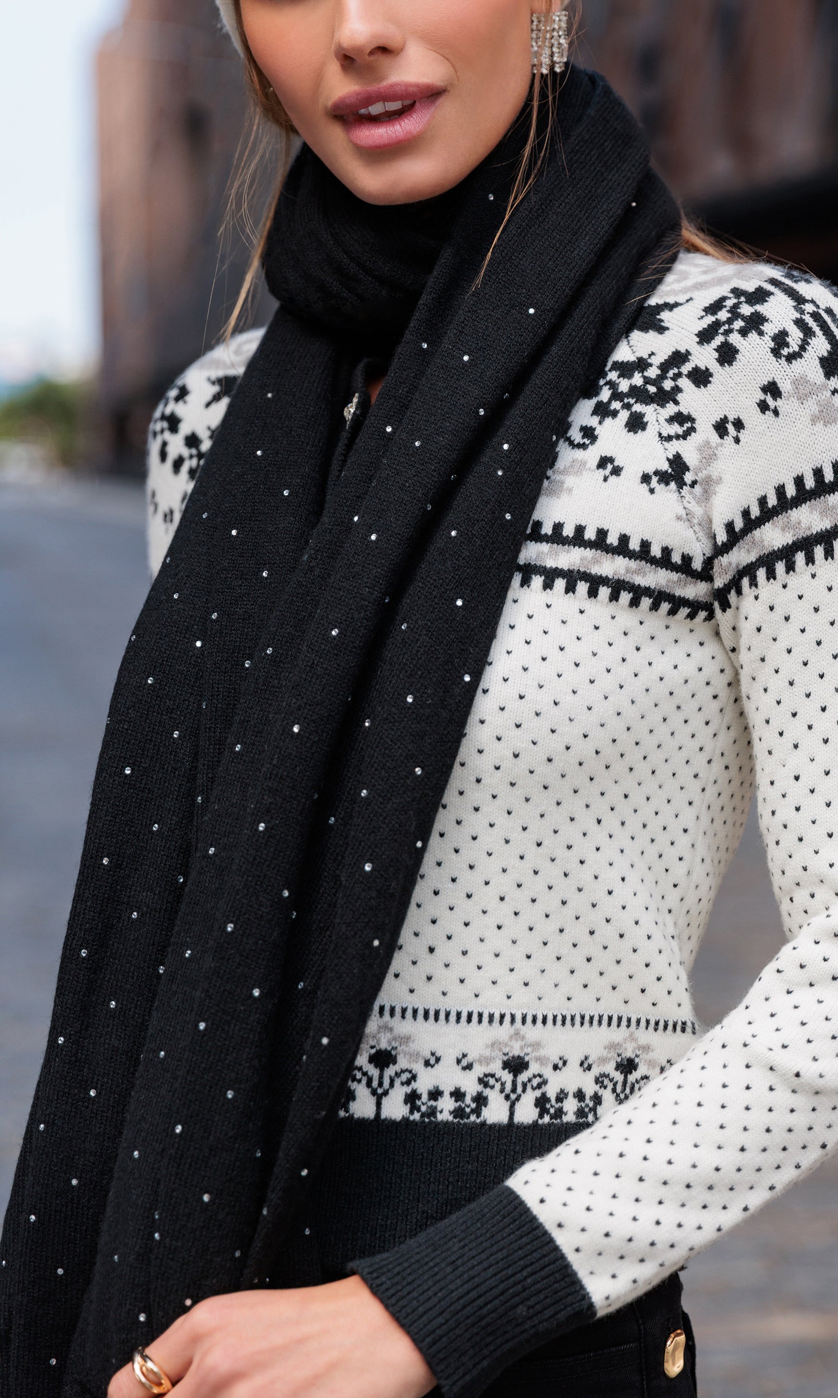Person wearing a black scarf and patterned white sweater outdoors