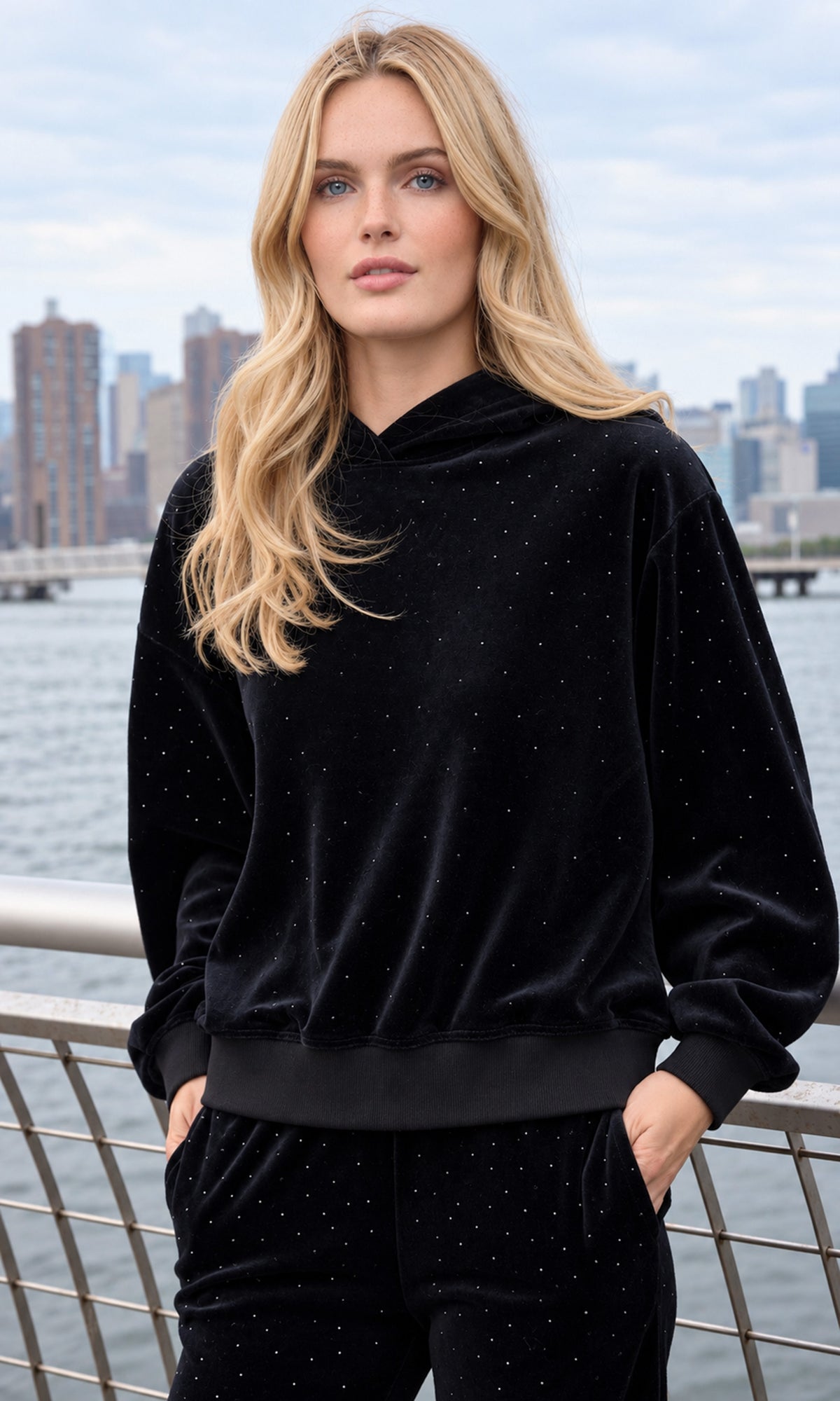 A blonde woman wearing a black velvet hoodie sweatshirt and matching sweatpants with subtle rhinestone embellishments.