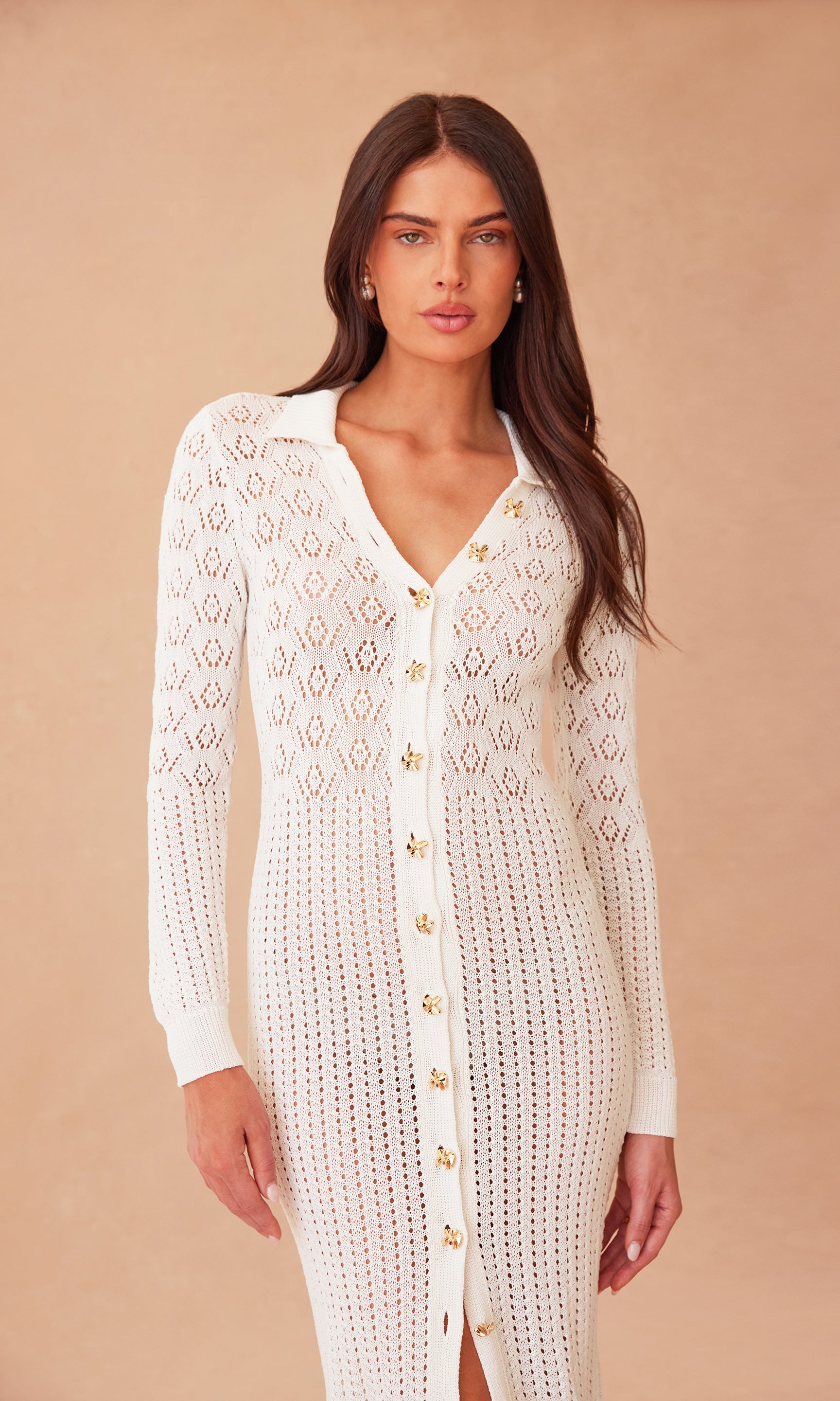 zoomed in image of model standing in front of a sandy peach wall, wearing the Eleni dress in white