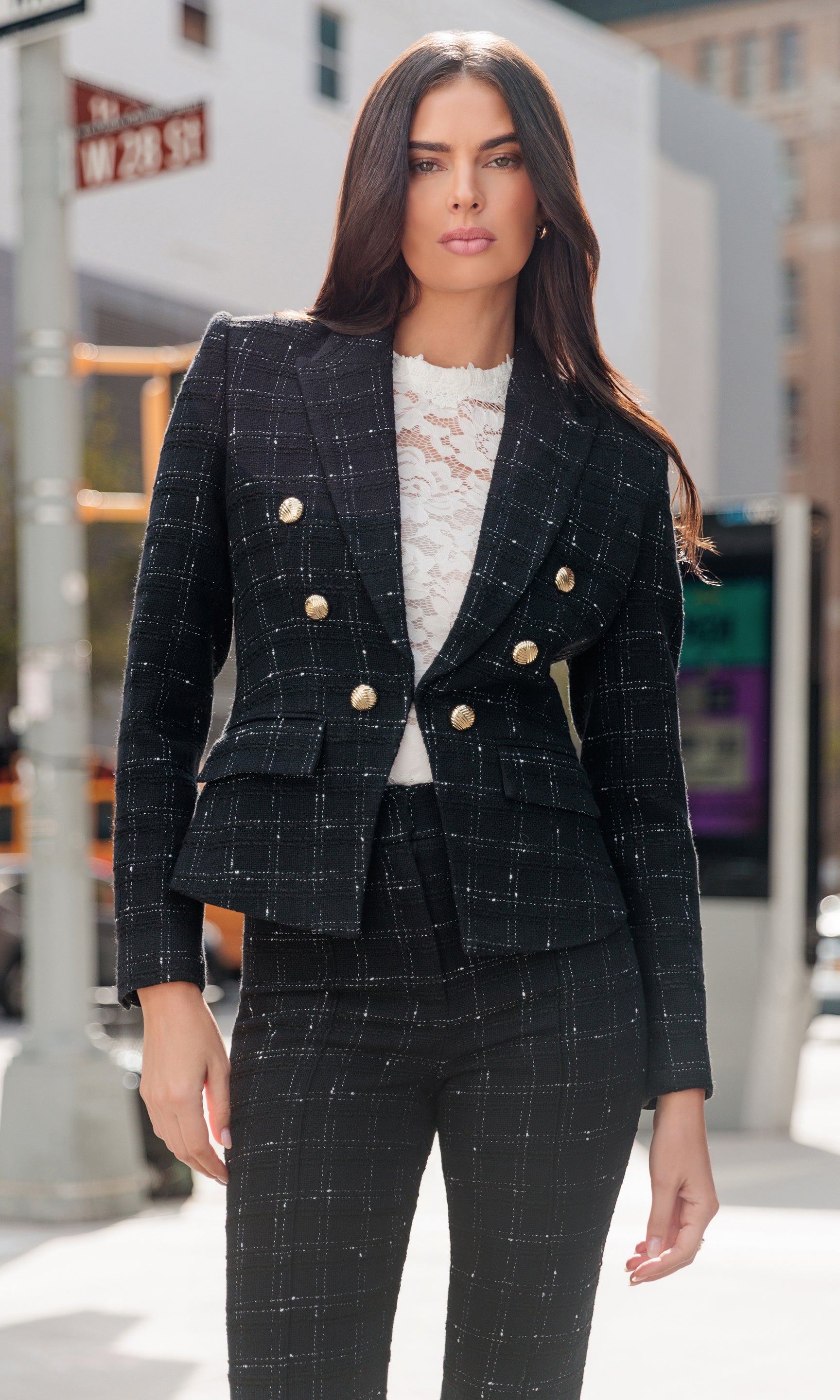 Woman wearing a black checkered suit with gold buttons on a city street.