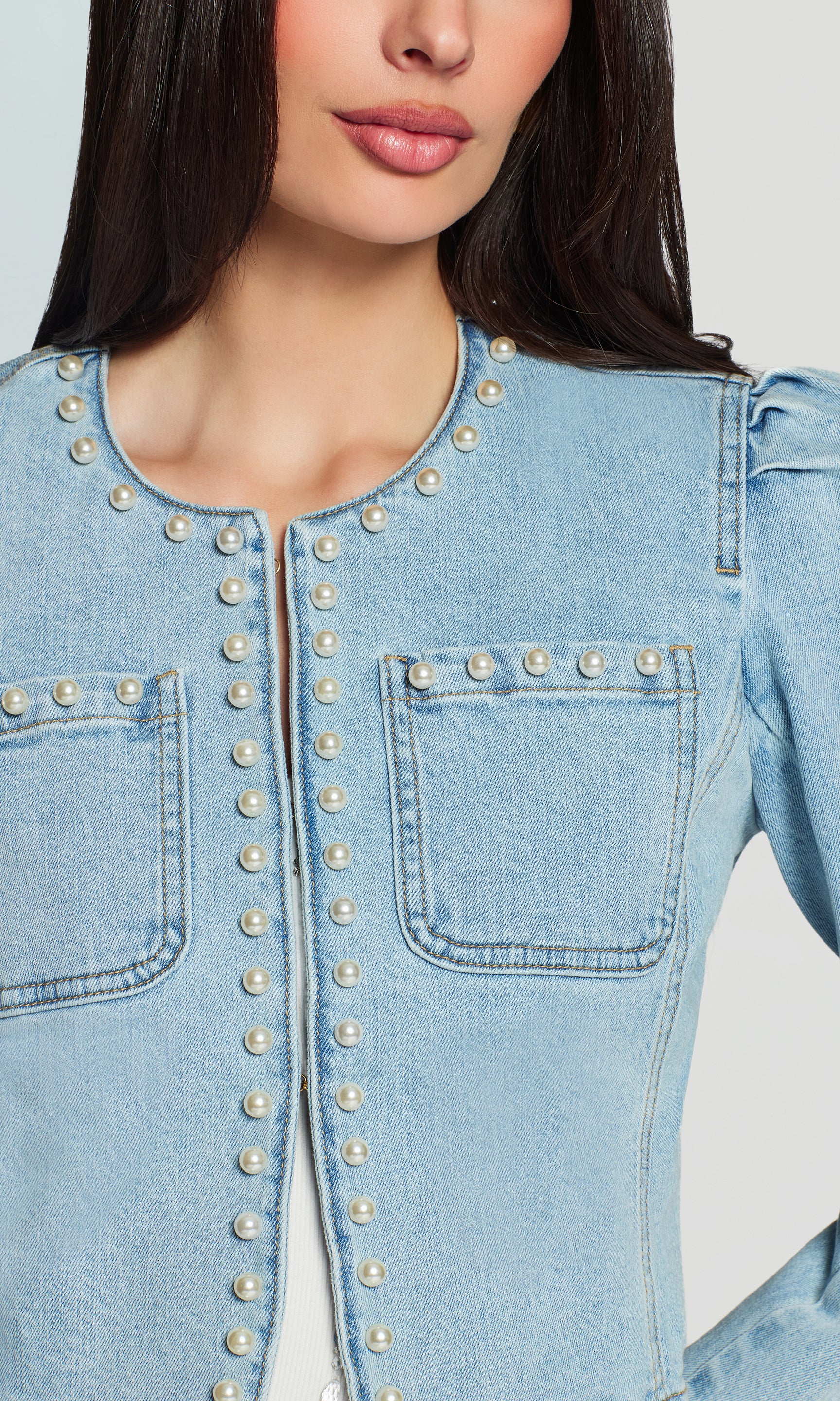 Close-up of light blue denim jacket with pearl embellishments on a white background