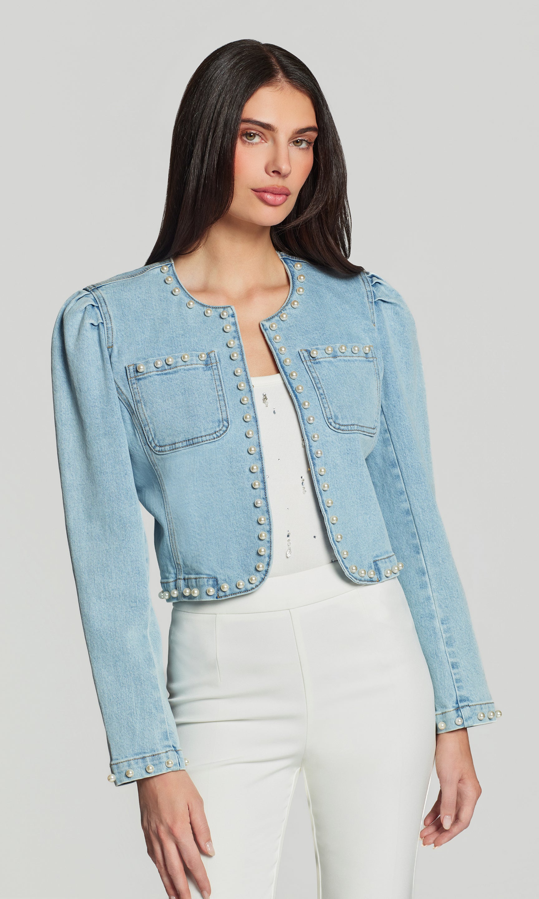 Woman wearing a light blue denim jacket with pearl embellishments on a gray background