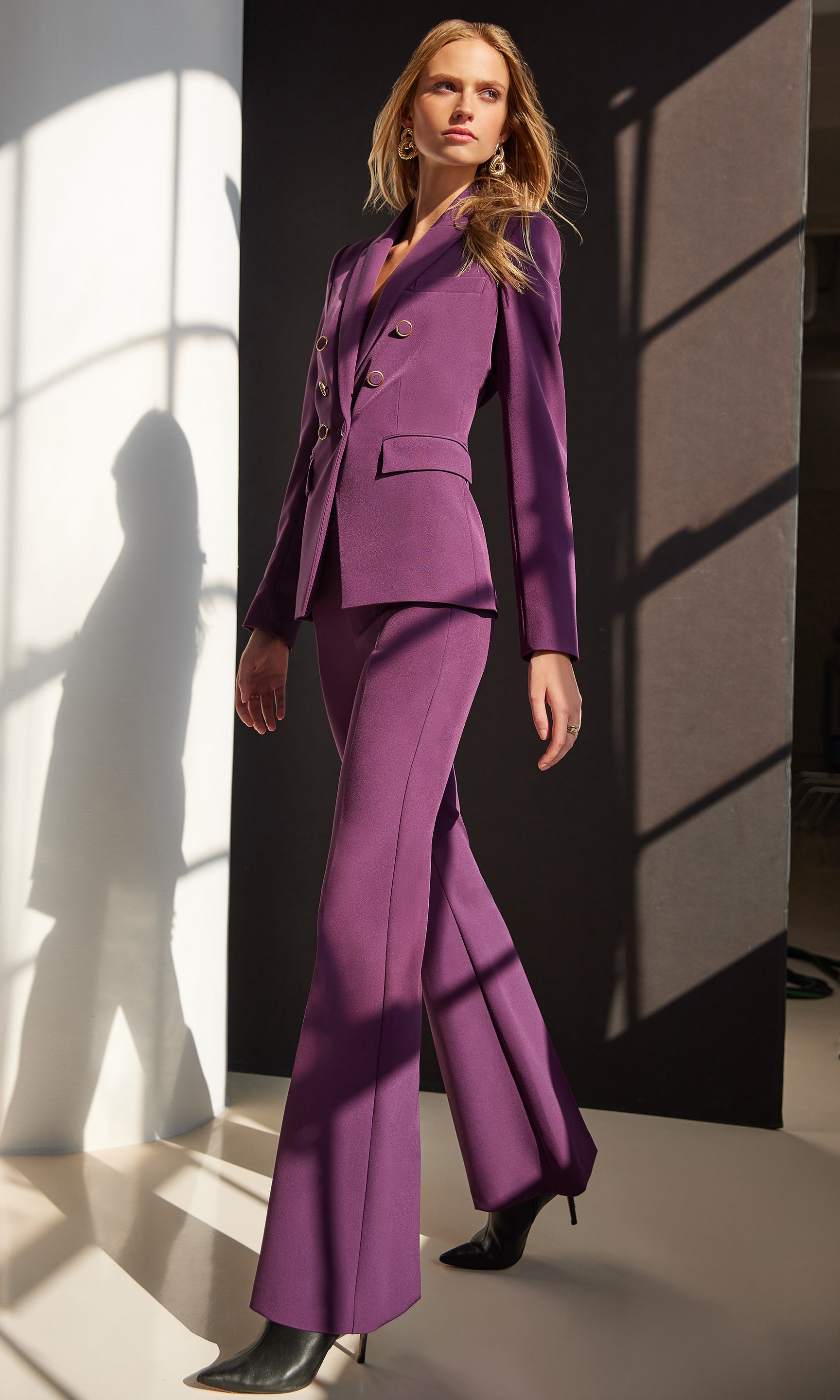 Woman wearing a purple suit standing against a black and white striped wall.