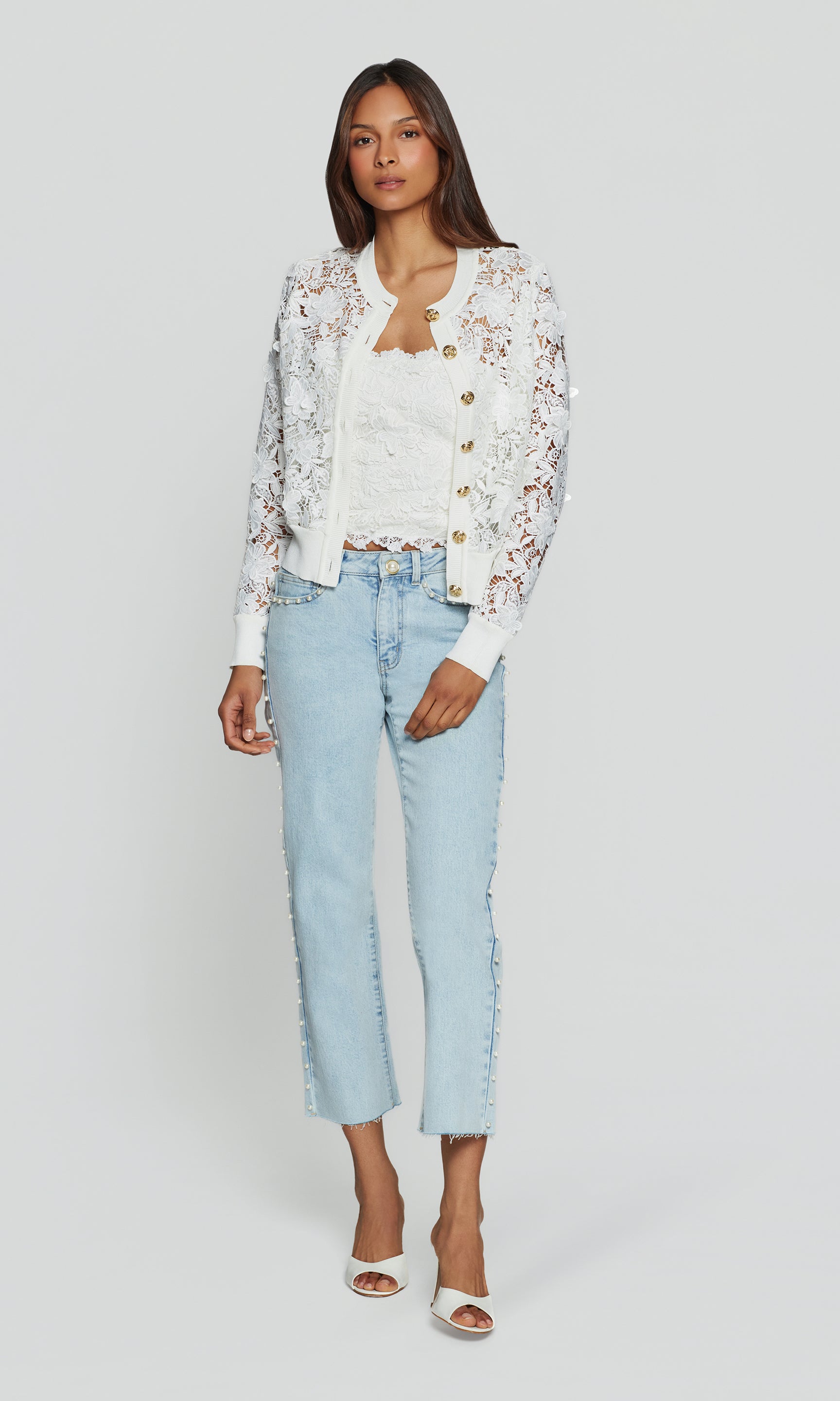 Woman wearing a floral cardigan, white top, and light blue jeans on a plain background