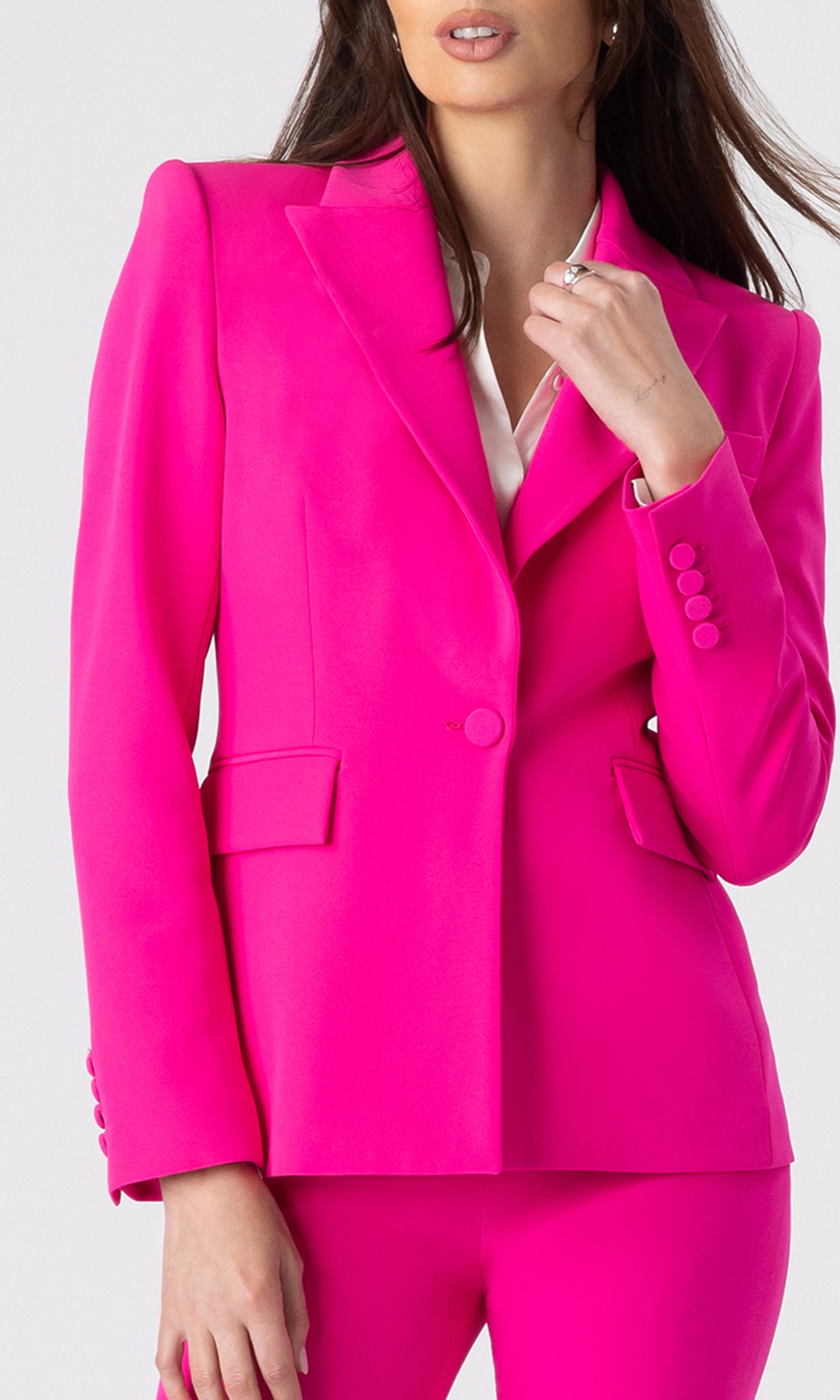 zoomed in image of model wearing a hot pink blazer with matching hot pink trousers and a white button-down shirt underneath, showcasing the structure details of the blazer