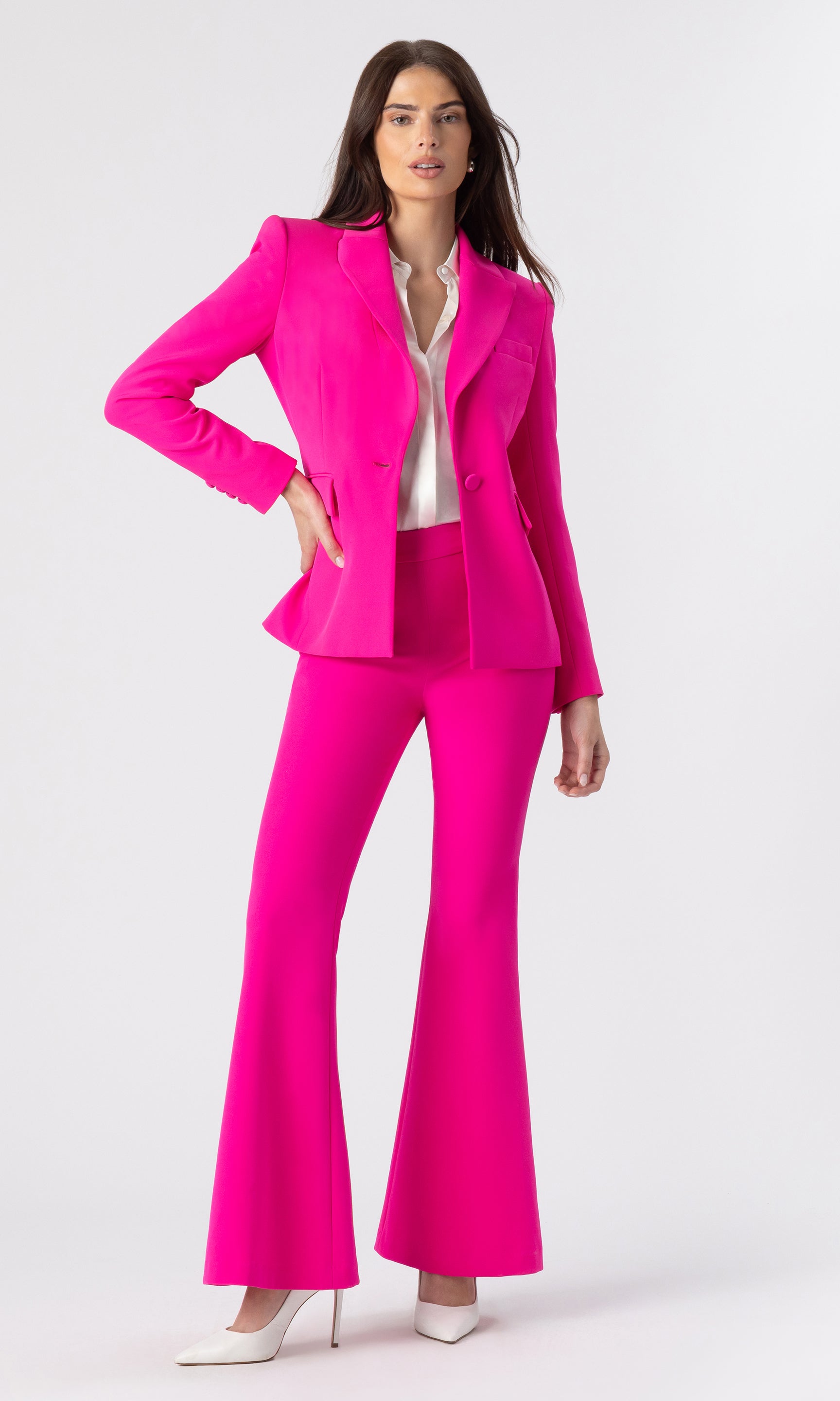 full body image of model posed with her hand on her hip wearing a hot pink blazer with matching hot pink trousers and a white button-down shirt underneath and white heels